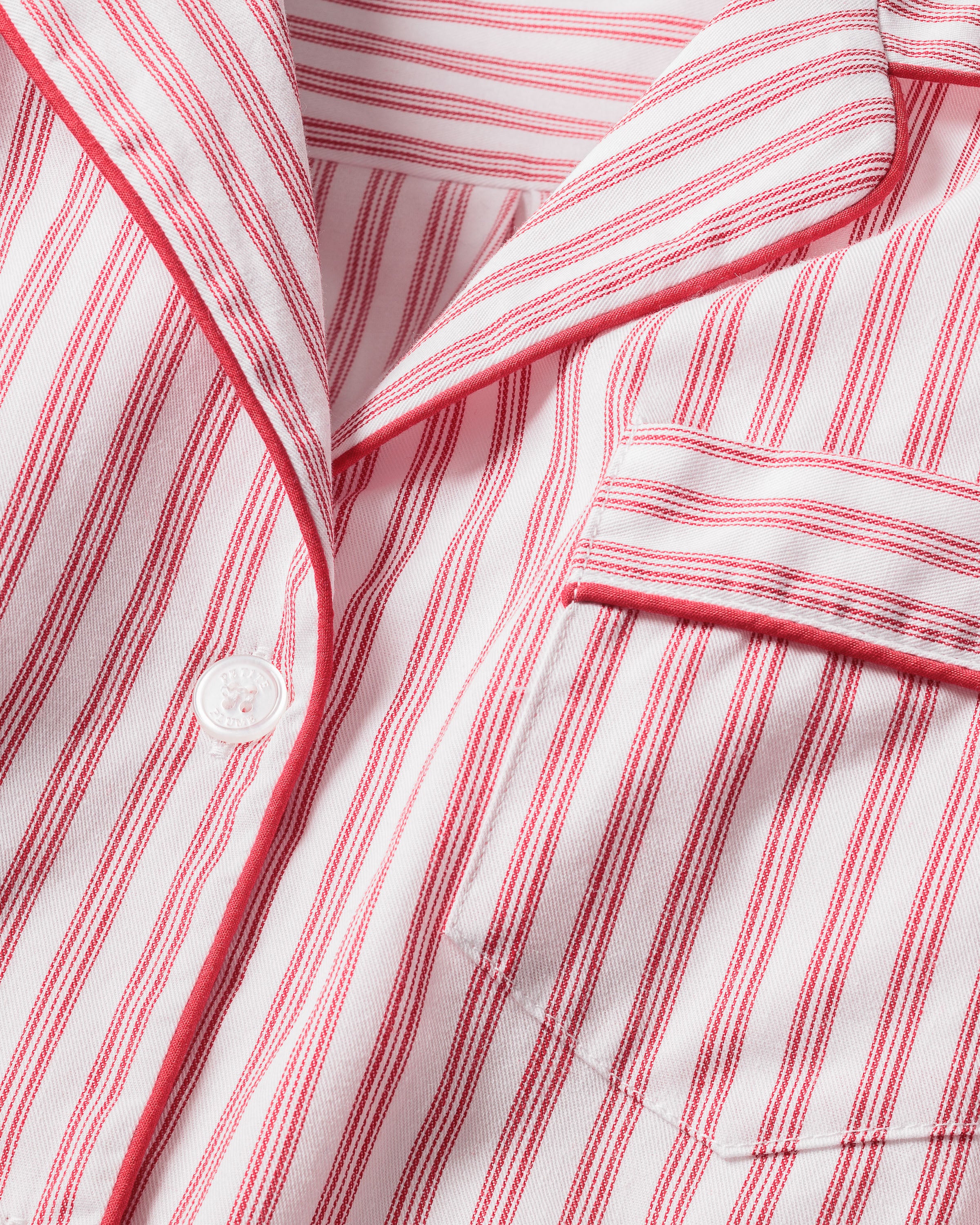 Close-up of Petite Plumes Mens Twill Pajama Set in Antique Red Ticking, featuring pink and white vertical stripes, a collar, a pocket with matching trim, and a single white button. Perfect for cozy relaxation.