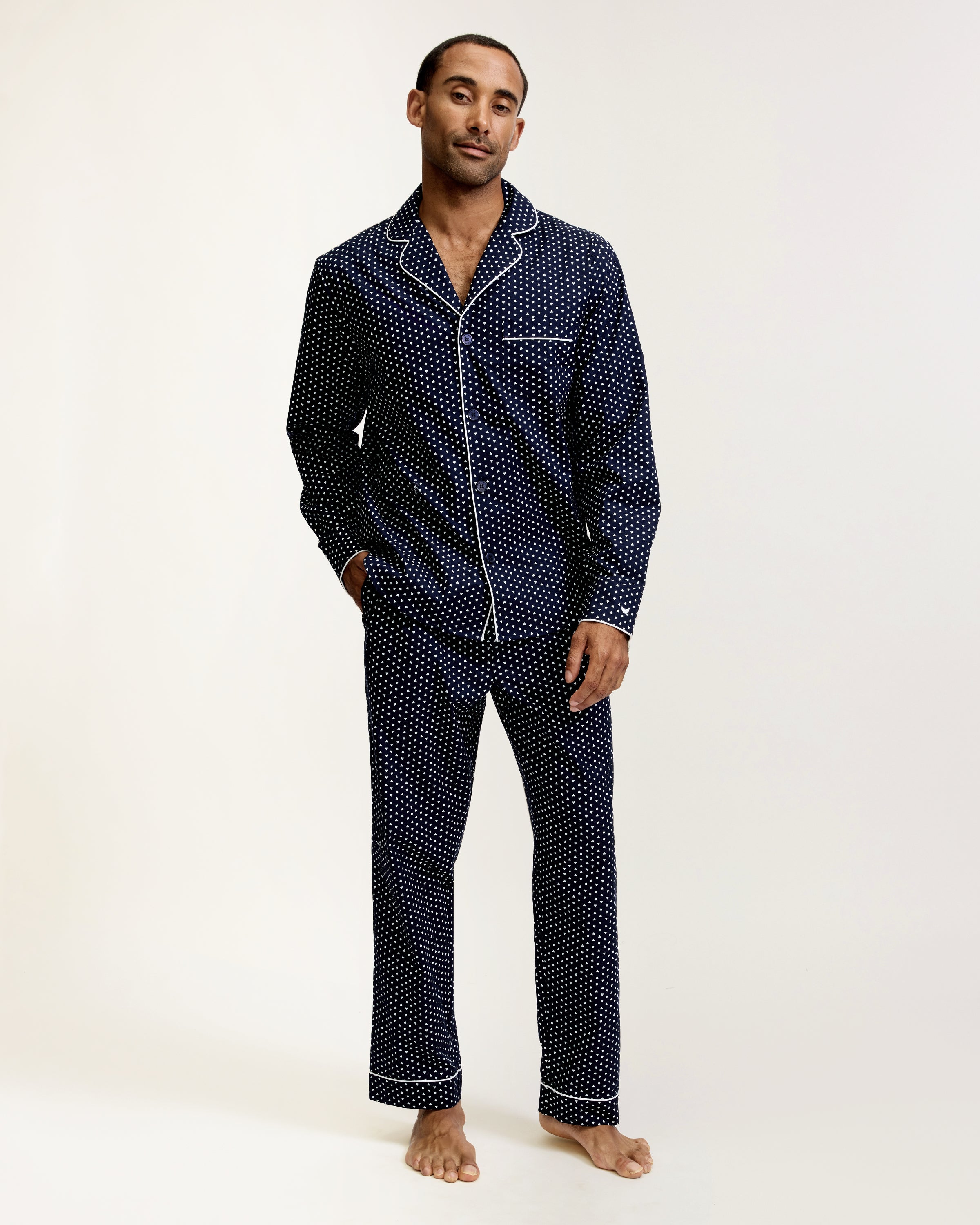 The Men's Twill Pajama Set in Midnight Hearts features a long-sleeve button-up top and pants, both navy blue with a small white polka dot pattern and white piping details.
