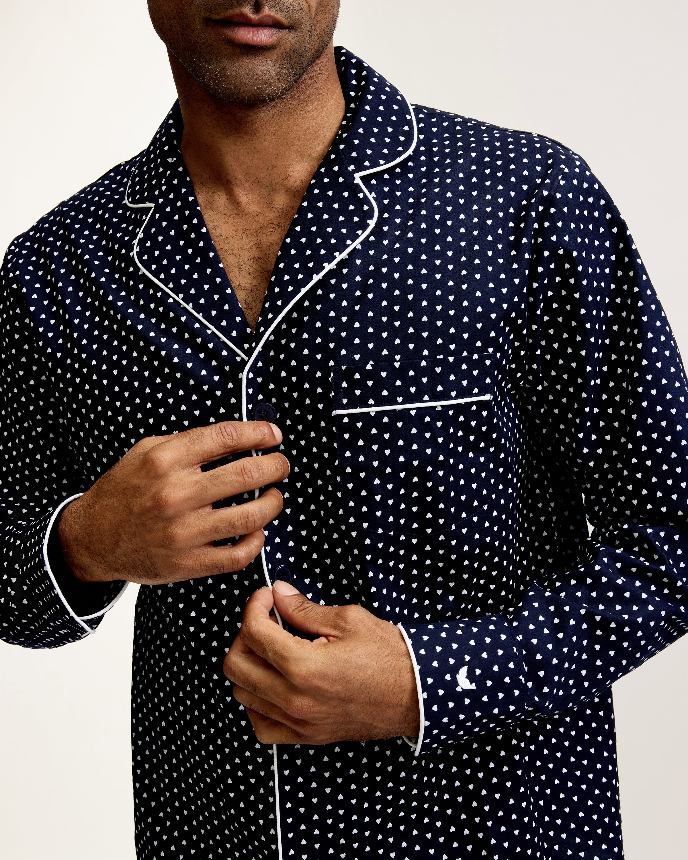 The Men's Twill Pajama Set in Midnight Hearts features a long-sleeve button-up top and pants, both navy blue with a small white polka dot pattern and white piping details.