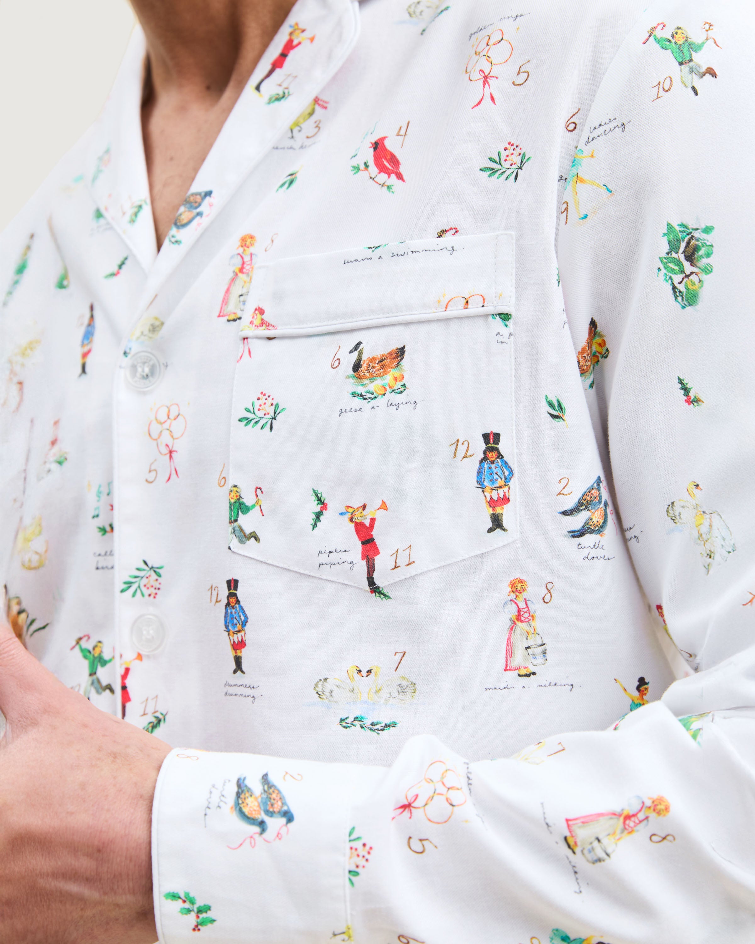 Men's Twill Pajama Set in 12 Days of Christmas: white button-up top and matching pants with a festive print featuring playful animals, palm trees, and people in various poses scattered across the fabric.