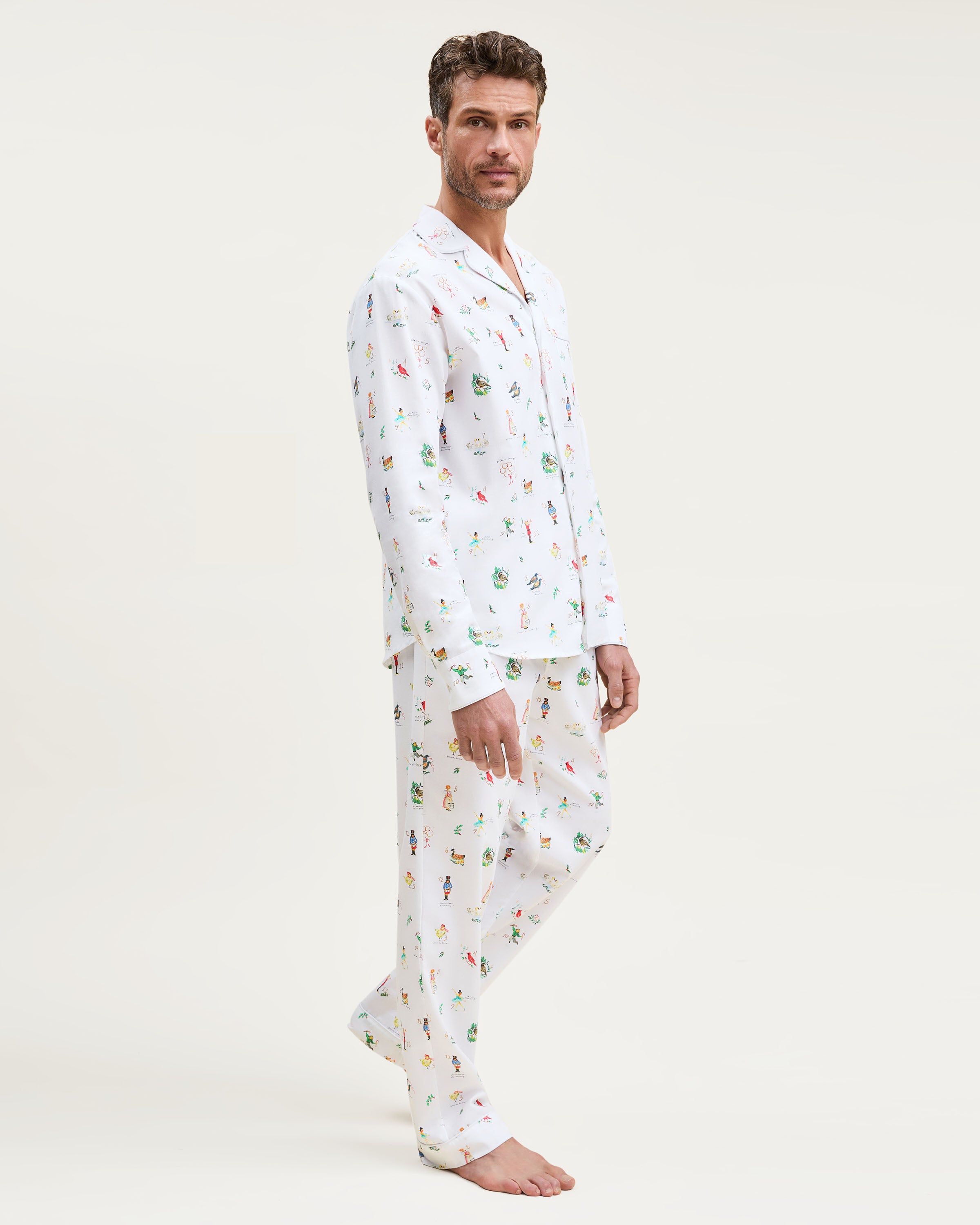 Men's Twill Pajama Set in 12 Days of Christmas: white button-up top and matching pants with a festive print featuring playful animals, palm trees, and people in various poses scattered across the fabric.