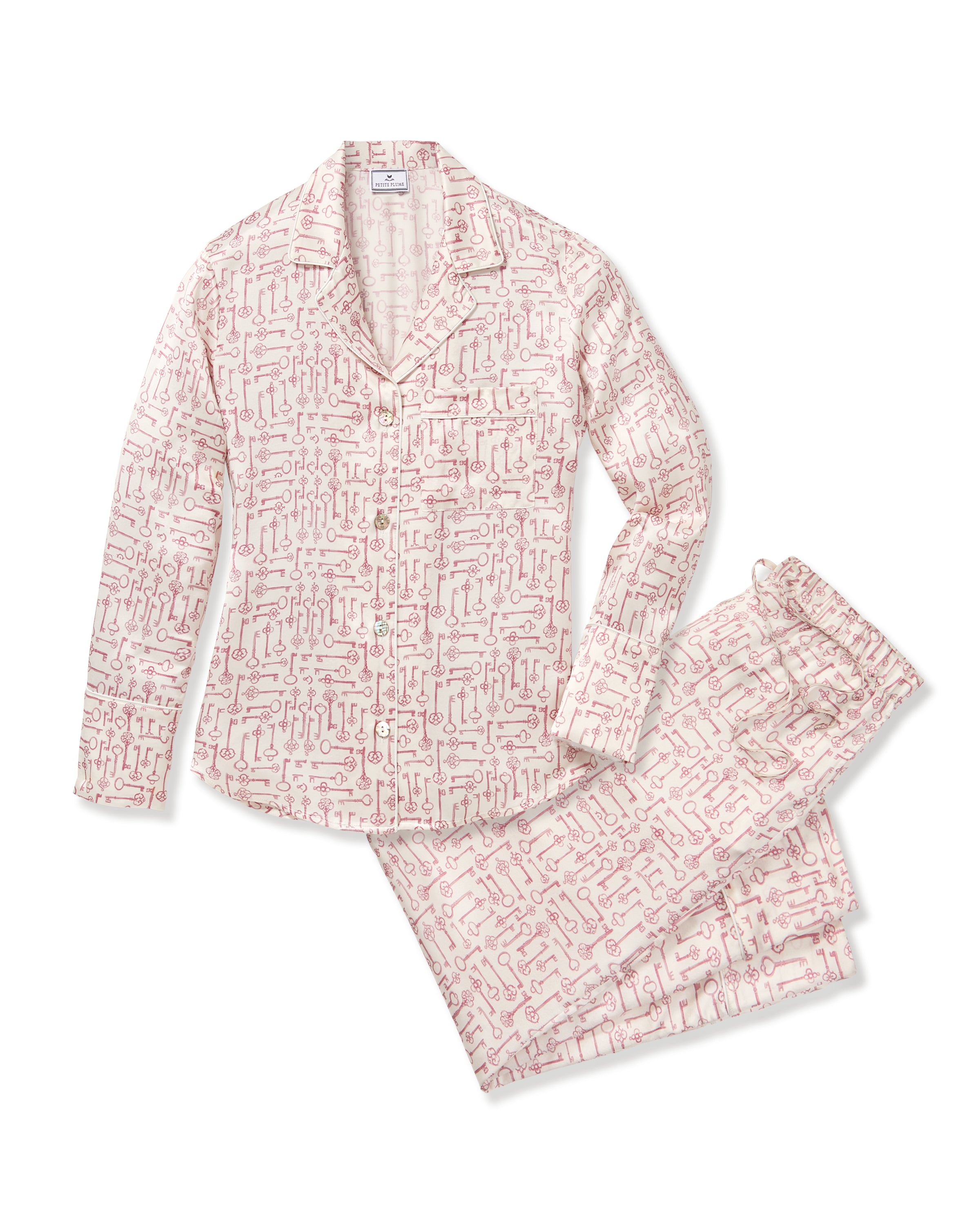 The Women's Silk Pajama Set in Key to My Heart features long-sleeve, button-up pajamas and matching pants in white silk with a pink wrench pattern, displayed flat on a white background.