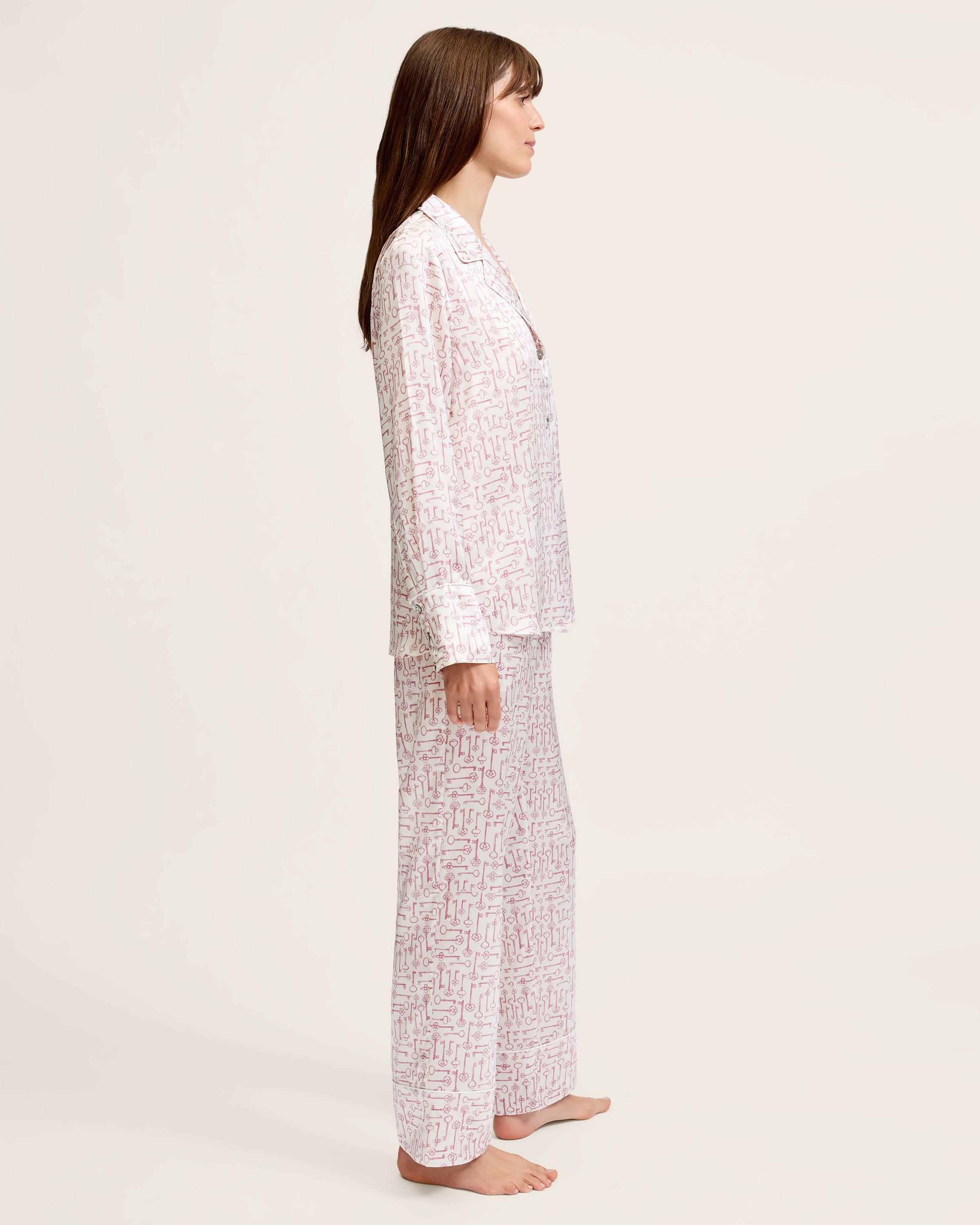 The Women's Silk Pajama Set in Key to My Heart features long-sleeve, button-up pajamas and matching pants in white silk with a pink wrench pattern, displayed flat on a white background.