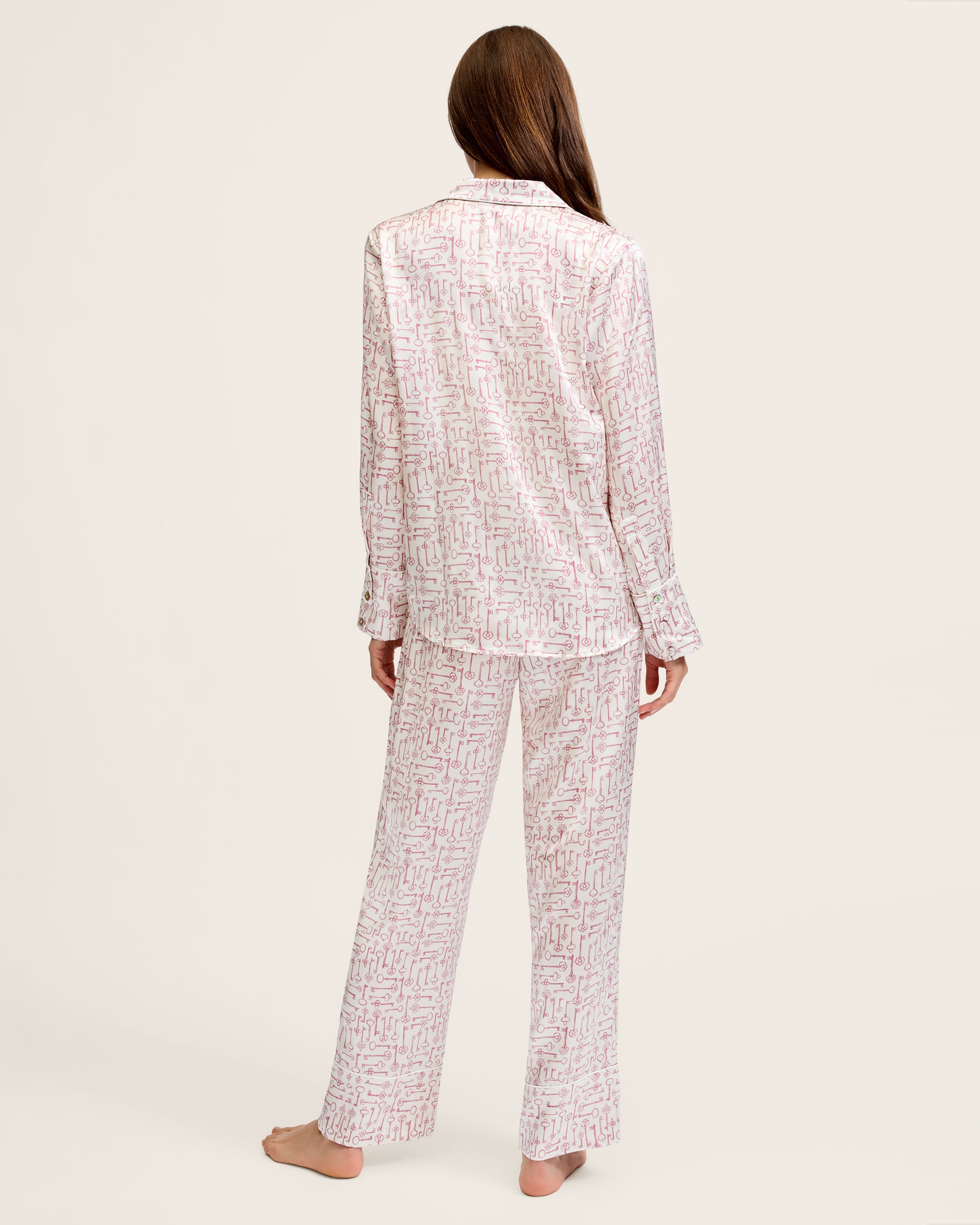 The Women's Silk Pajama Set in Key to My Heart features long-sleeve, button-up pajamas and matching pants in white silk with a pink wrench pattern, displayed flat on a white background.