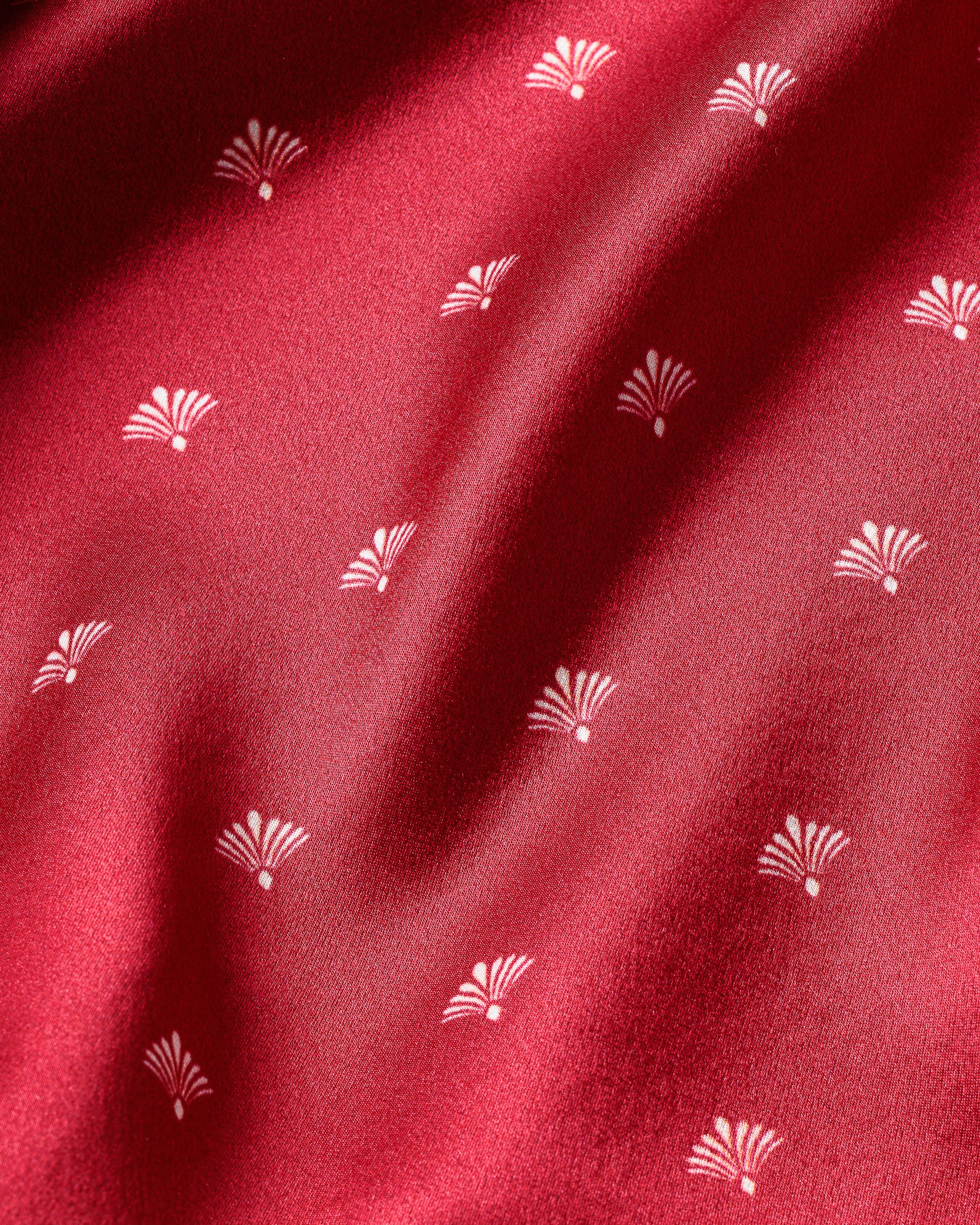 Close-up of the Womens Silk Cami Short Set in Crimson Art Nouveau by Petite Plume, showcasing red luxury fabric with small white fan-shaped patterns. The smooth silk texture and subtle folds evoke gentle shadows like an Art Nouveau print.