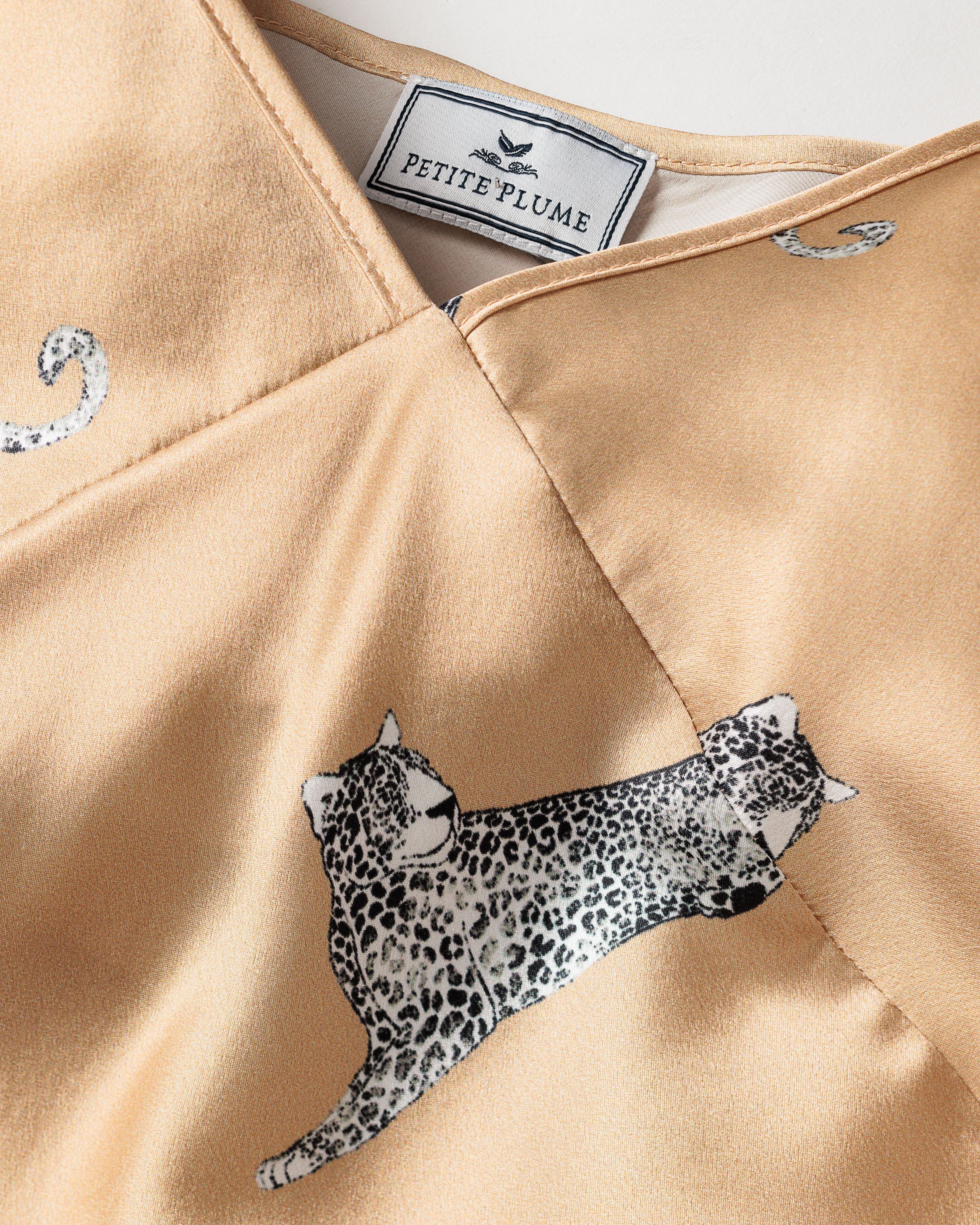 A close-up of the Womens Silk Cami Short Set in Panthère Champagne by Petite Plume reveals a beige fabric with black and white leopard print, featuring two leopards and swirling patterns. Crafted from luxurious Mulberry silk.