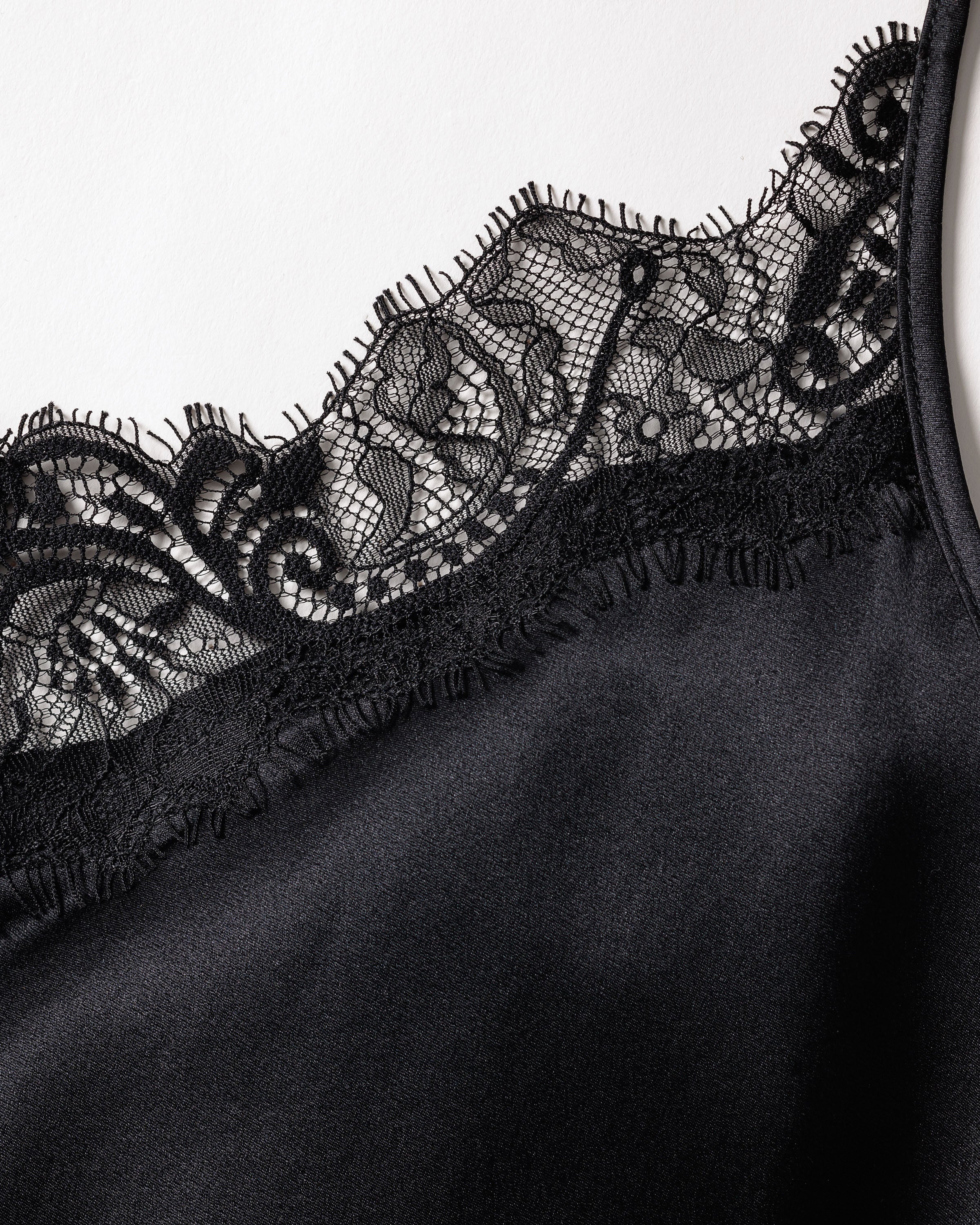 Close-up of the Womens Silk Lace Cami Short Set in Black by Petite Plume, showcasing black, silky luxury sleepwear with intricate floral lace detailing along the edge for an elegant and delicate touch to this machine-washable silk garment.
