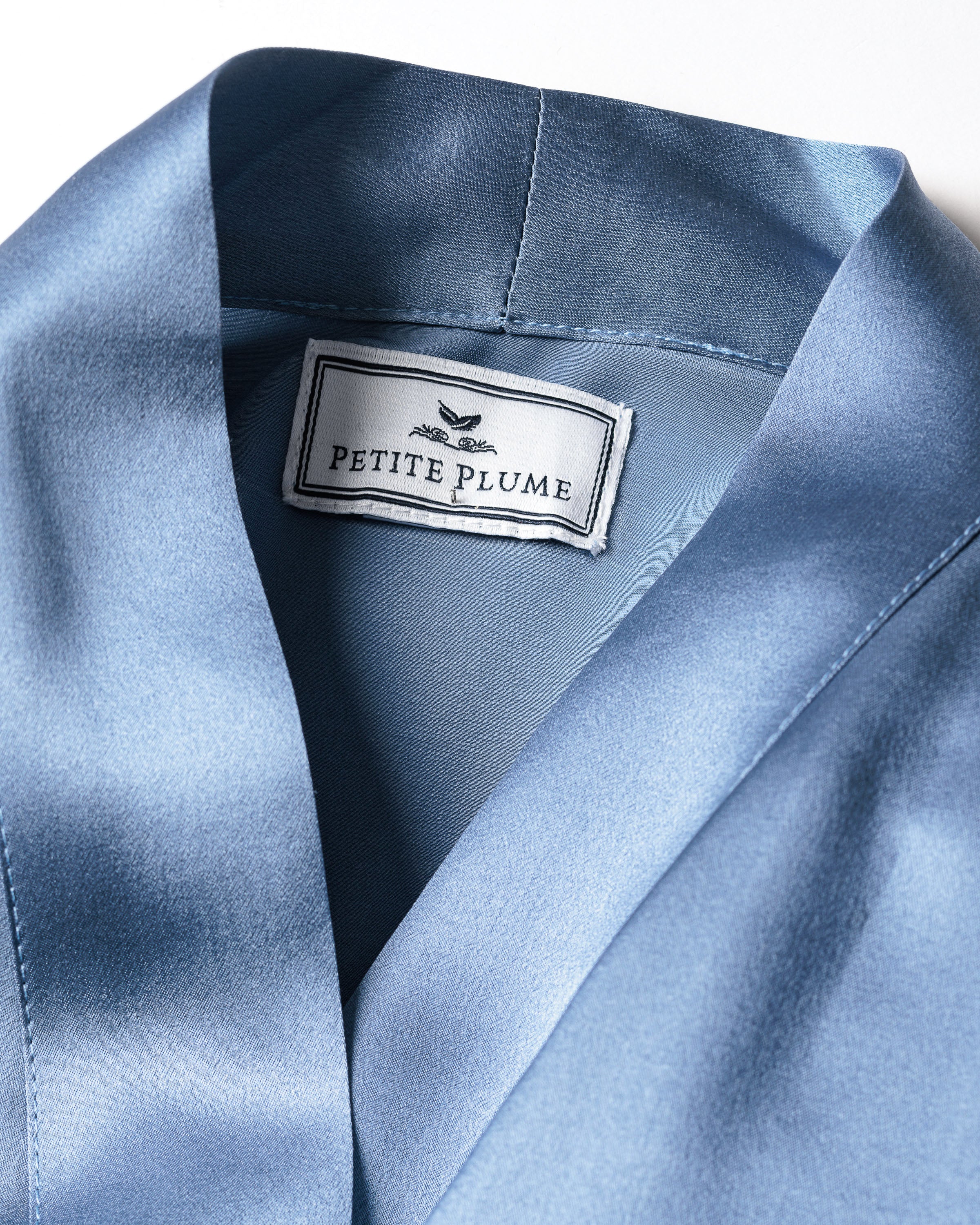Close-up of the Womens Silk Lace Robe in Mystique Blue by Petite Plume, showcasing a label inside the collar. The garments smooth, shiny texture emulates luxurious Mulberry Silk and is hypoallergenic.