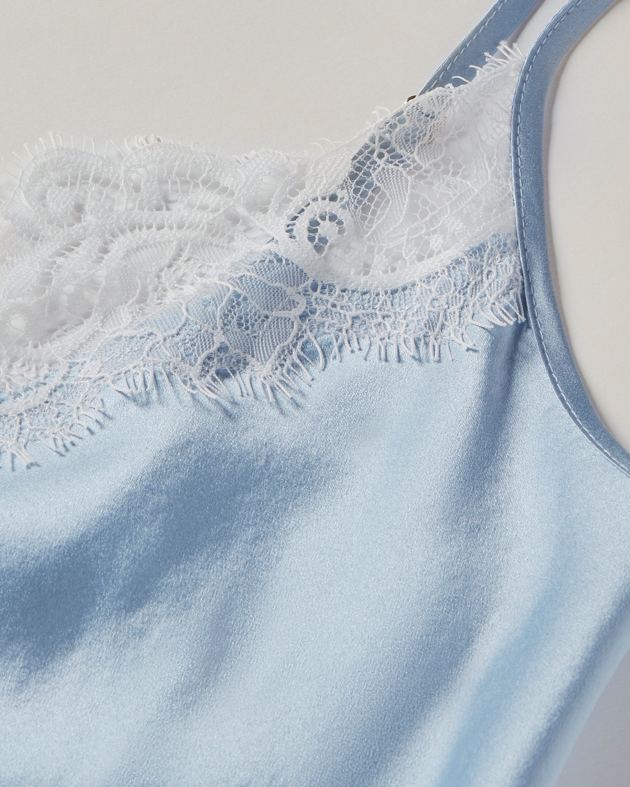 A close-up of a luxury sleepwear item: Petite Plumes Womens Silk Lace Slip Dress in Periwinkle, featuring delicate white lace trim at the neckline, set against a neutral background.
