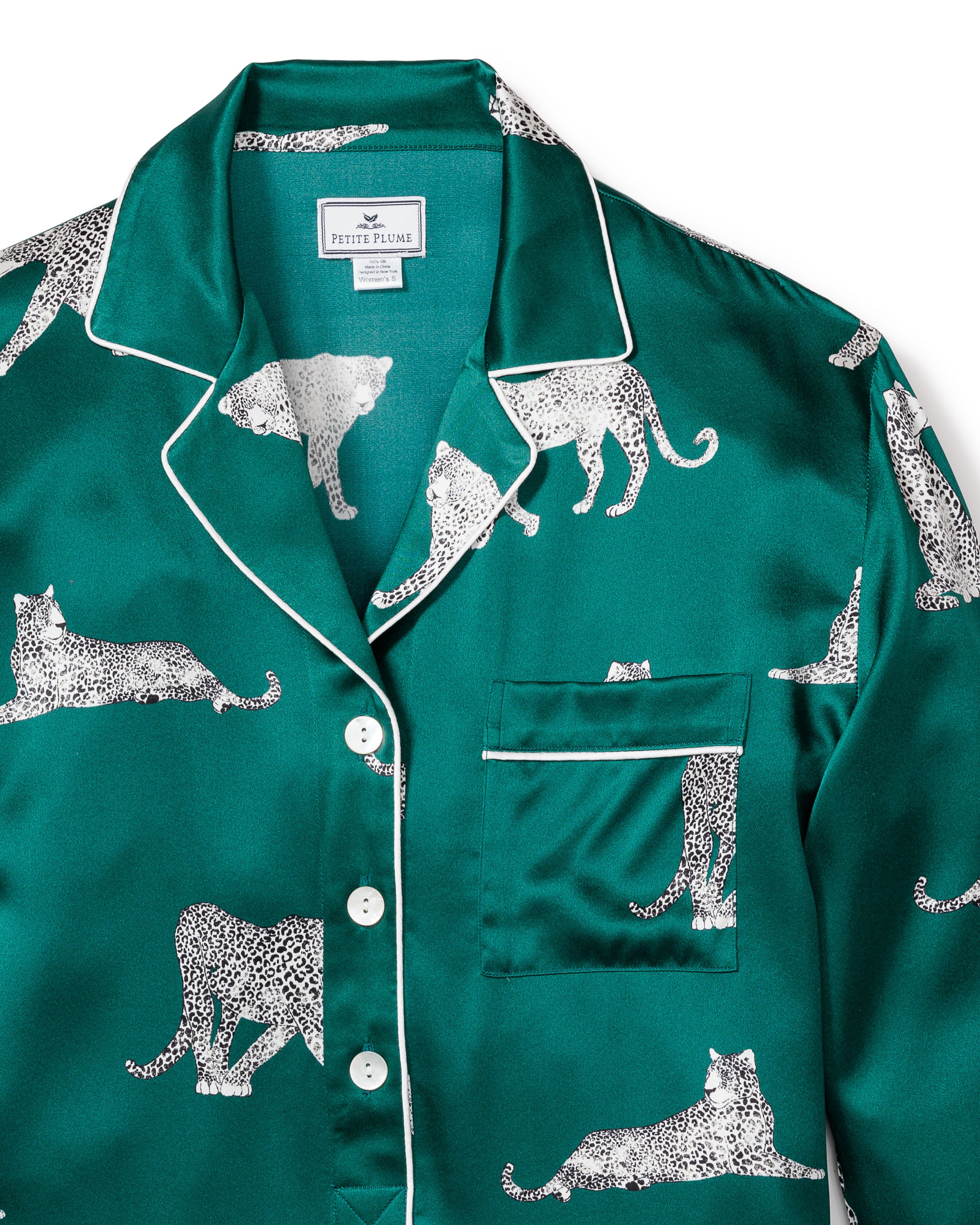 The Petite Plume Womens Silk Nightshirt in Panthère de Luxe features a luxurious green satin with white, black-spotted leopards pattern. It includes white piping, buttons, and a breast pocket on the left for ultimate comfort.