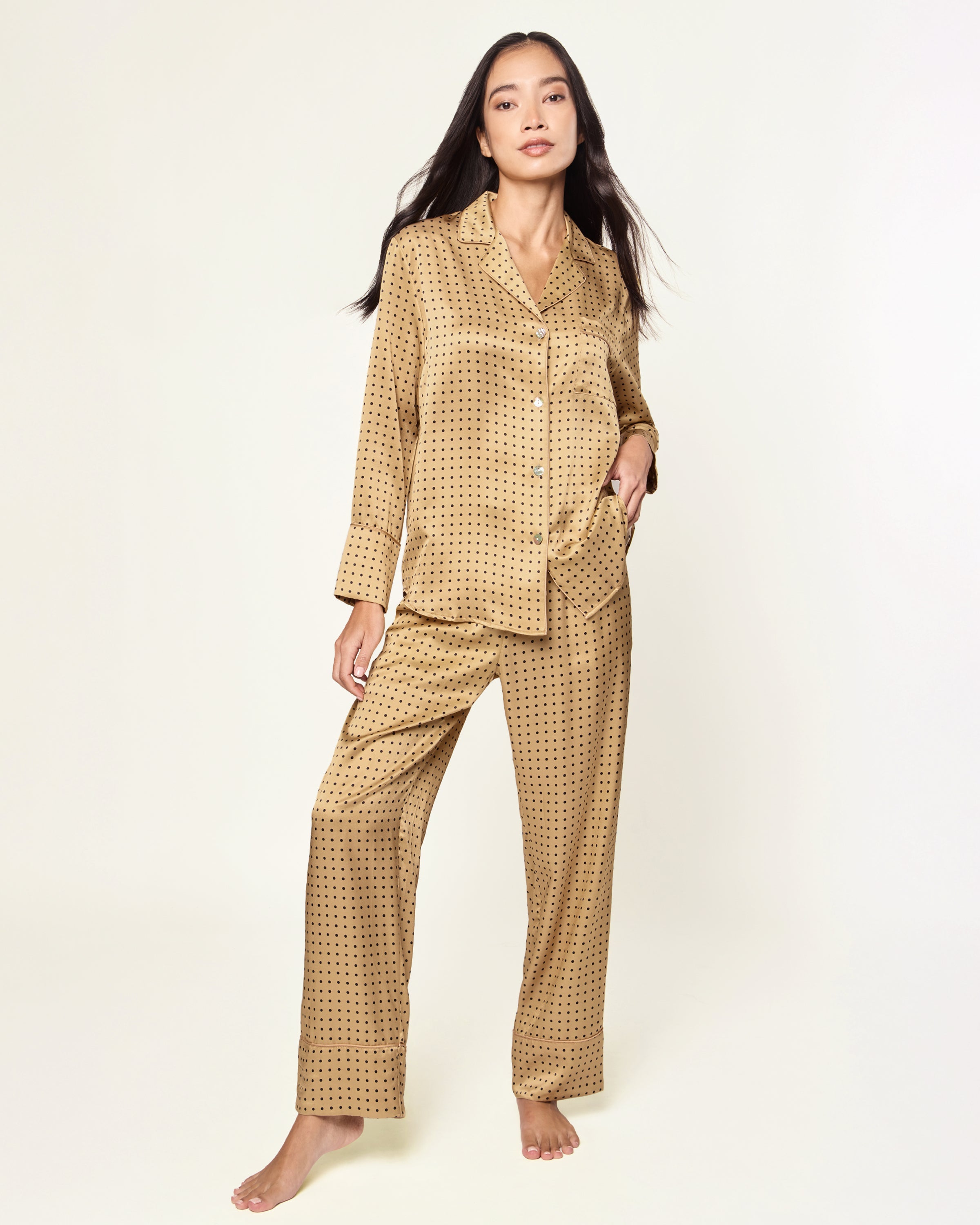 The Women's Silk Pajama Set features a gold fabric with black polka dots, including a long-sleeve button-up top with chest pocket and matching drawstring pants.