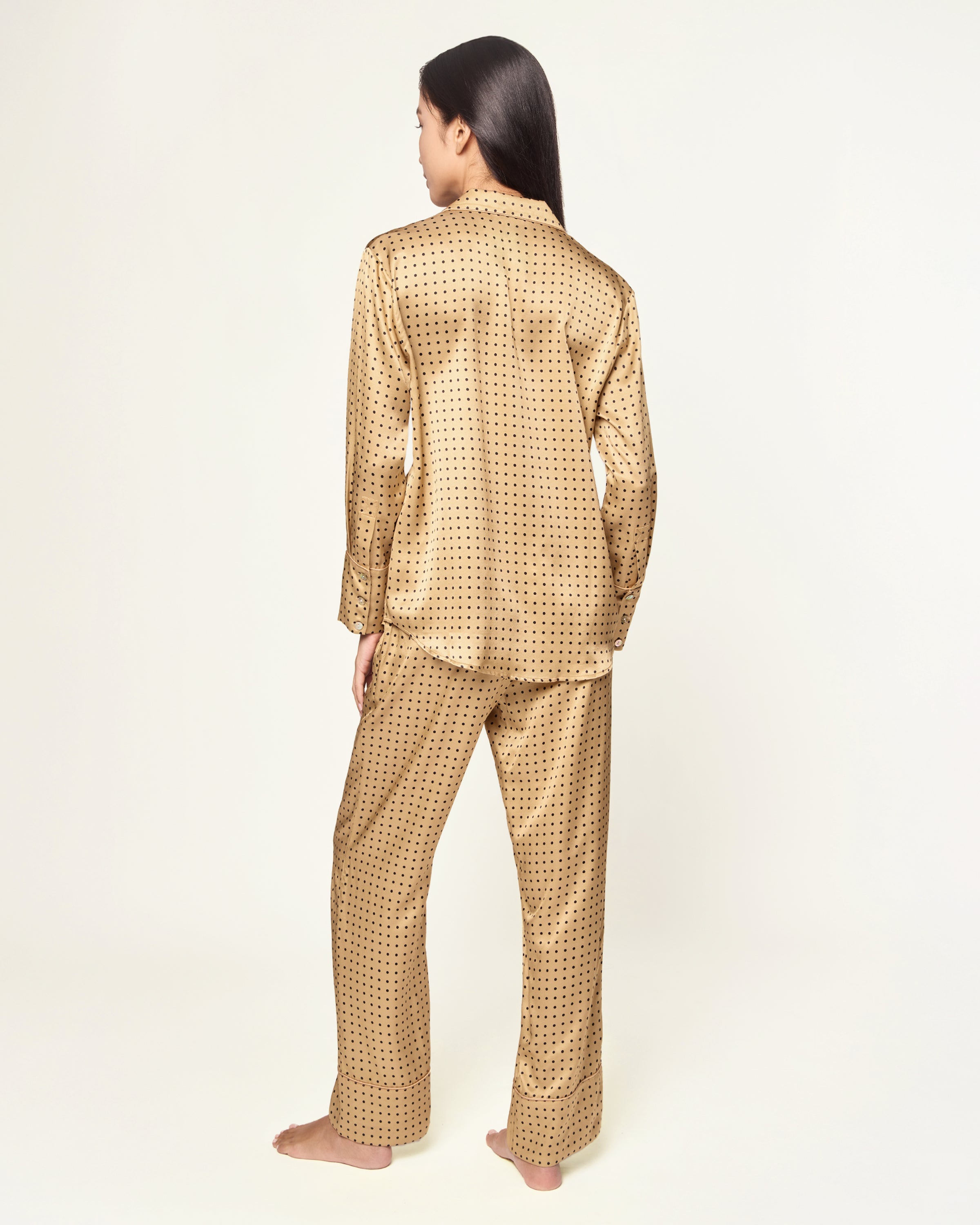 The Women's Silk Pajama Set features a gold fabric with black polka dots, including a long-sleeve button-up top with chest pocket and matching drawstring pants.