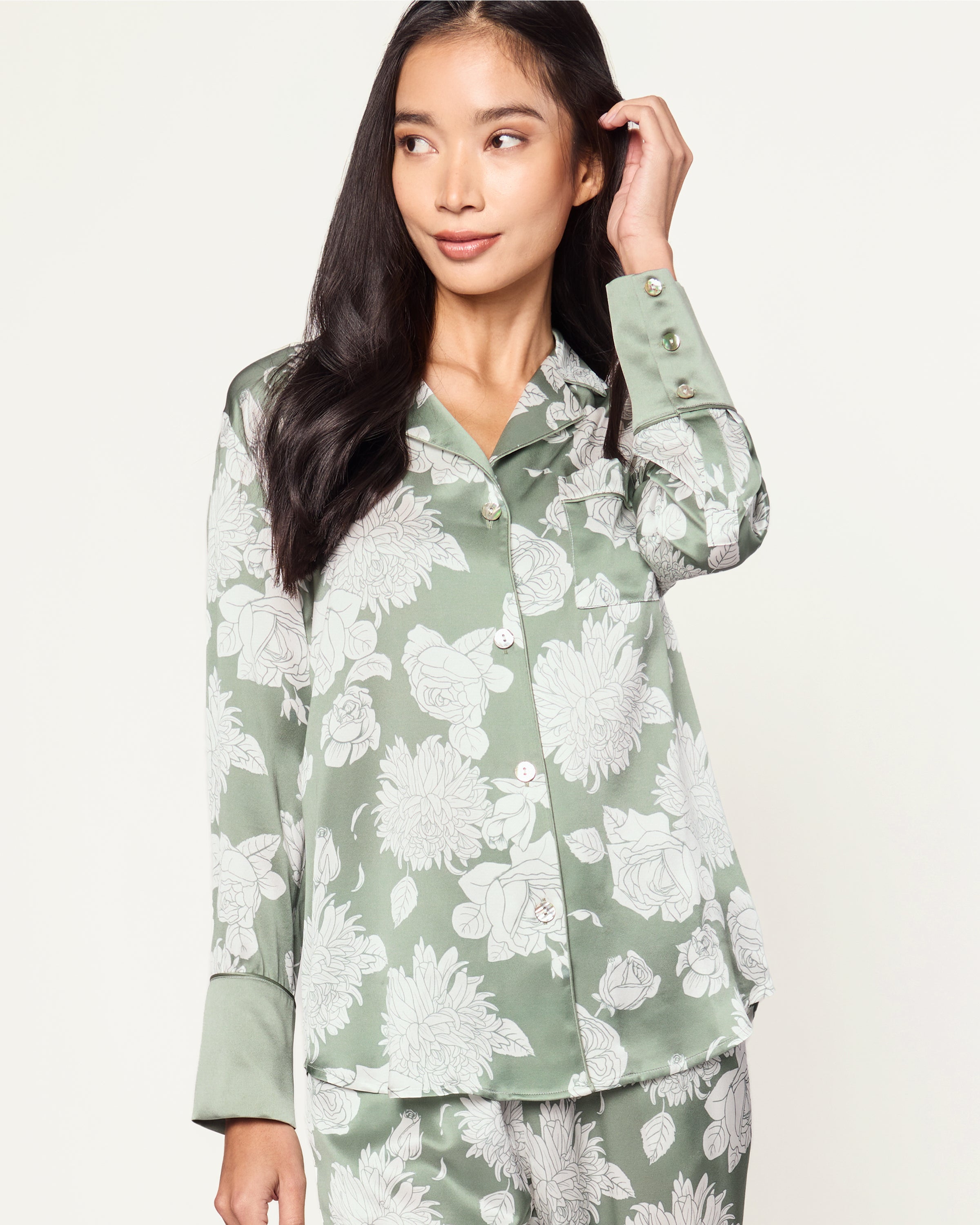Women's Silk Pajama Set in Sage Bloom: a sage green satin set with a white floral pattern, featuring a long-sleeve button-up top with chest pocket and matching drawstring pants.