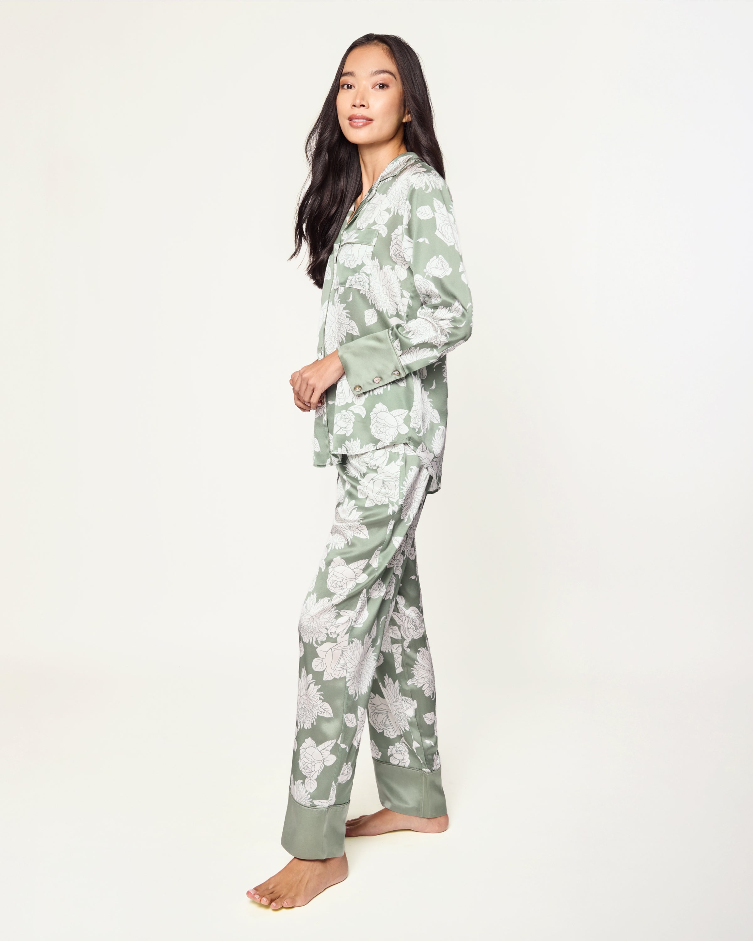 Women's Silk Pajama Set in Sage Bloom: a sage green satin set with a white floral pattern, featuring a long-sleeve button-up top with chest pocket and matching drawstring pants.