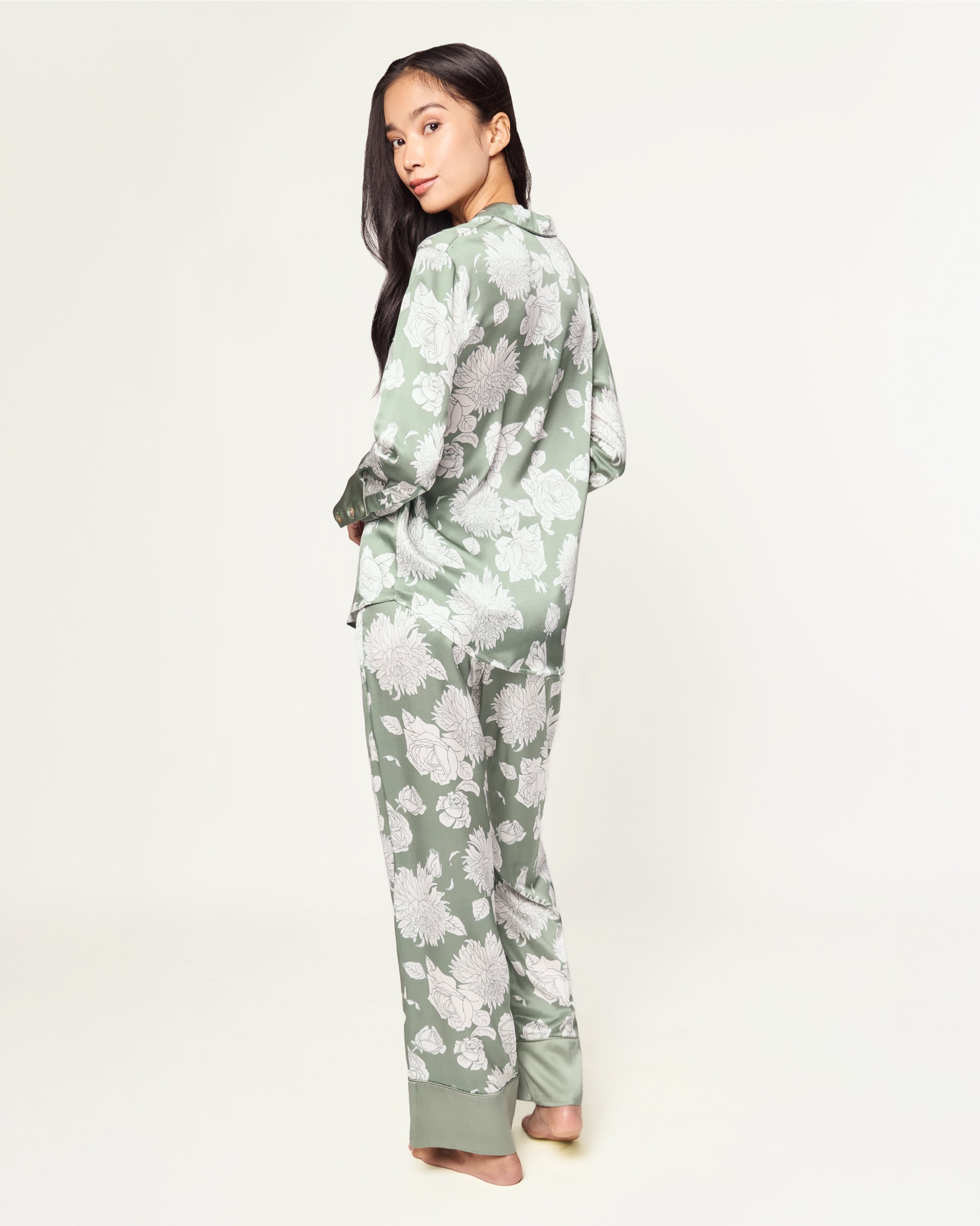 Women's Silk Pajama Set in Sage Bloom: a sage green satin set with a white floral pattern, featuring a long-sleeve button-up top with chest pocket and matching drawstring pants.