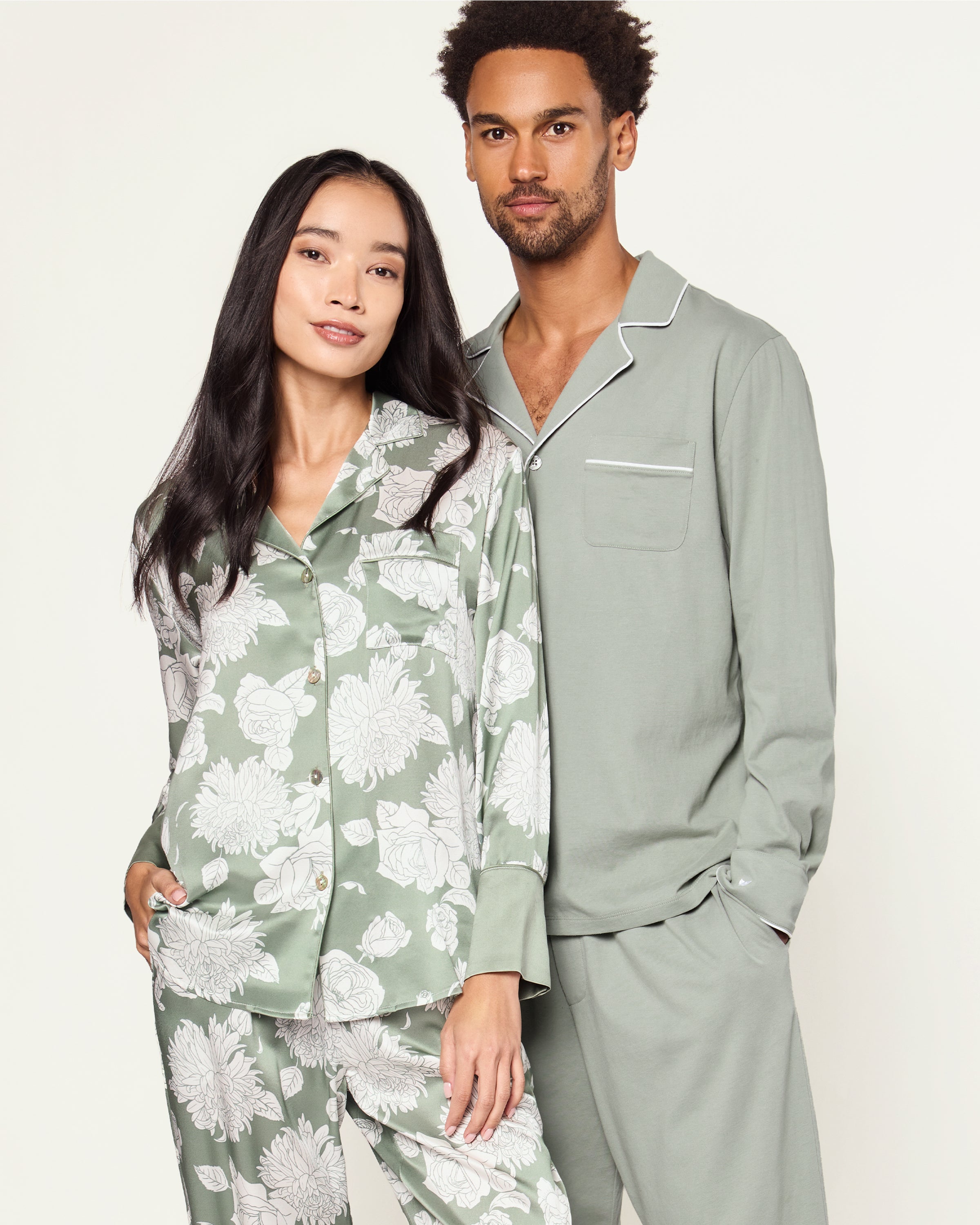 Women's Silk Pajama Set in Sage Bloom: a sage green satin set with a white floral pattern, featuring a long-sleeve button-up top with chest pocket and matching drawstring pants.