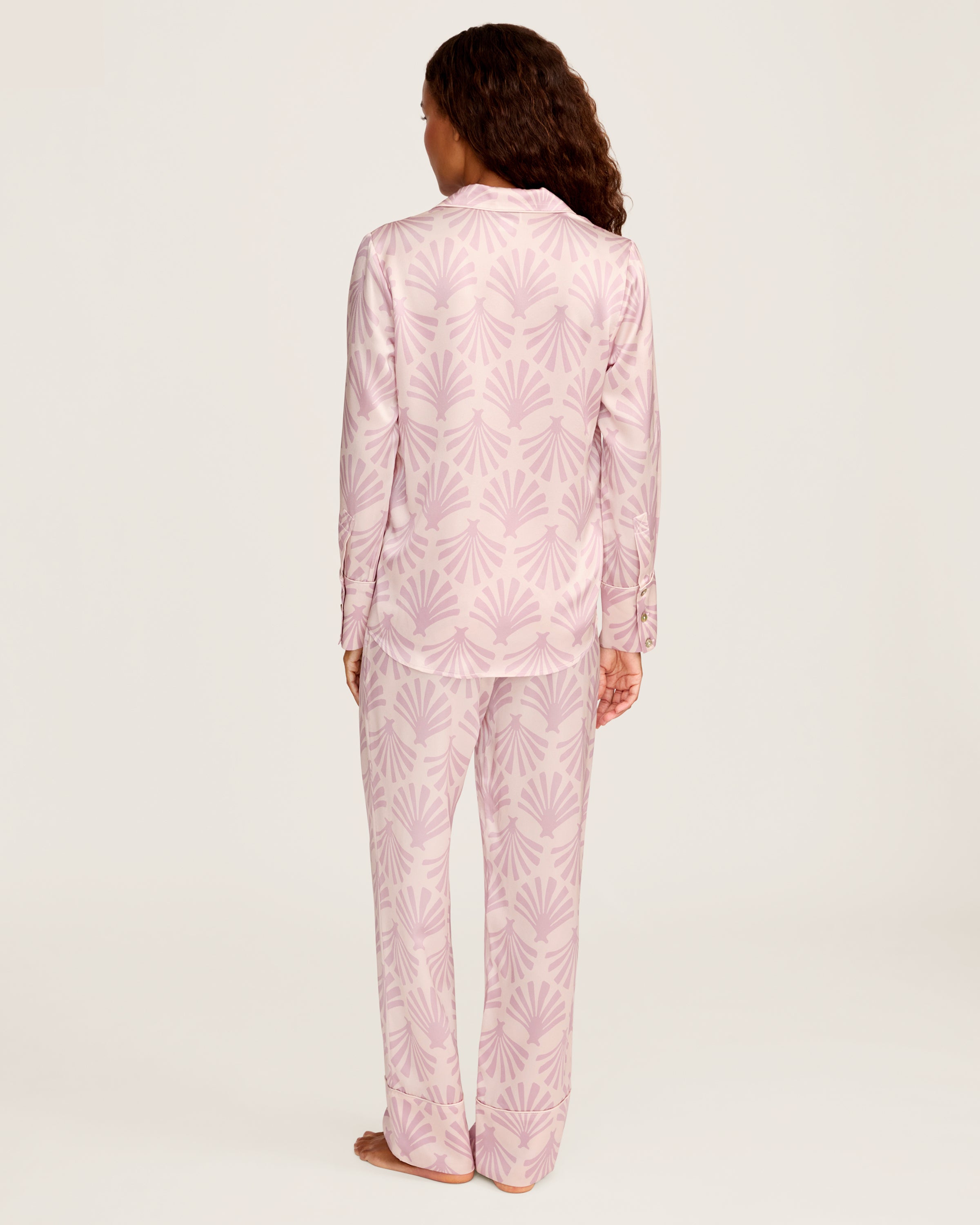 The Women's Silk Pajama Set in Blush Tide features pink long-sleeved, button-up top with collar and pocket, adorned with a blush and mauve geometric fan pattern, shown flat with matching pants beside the top.