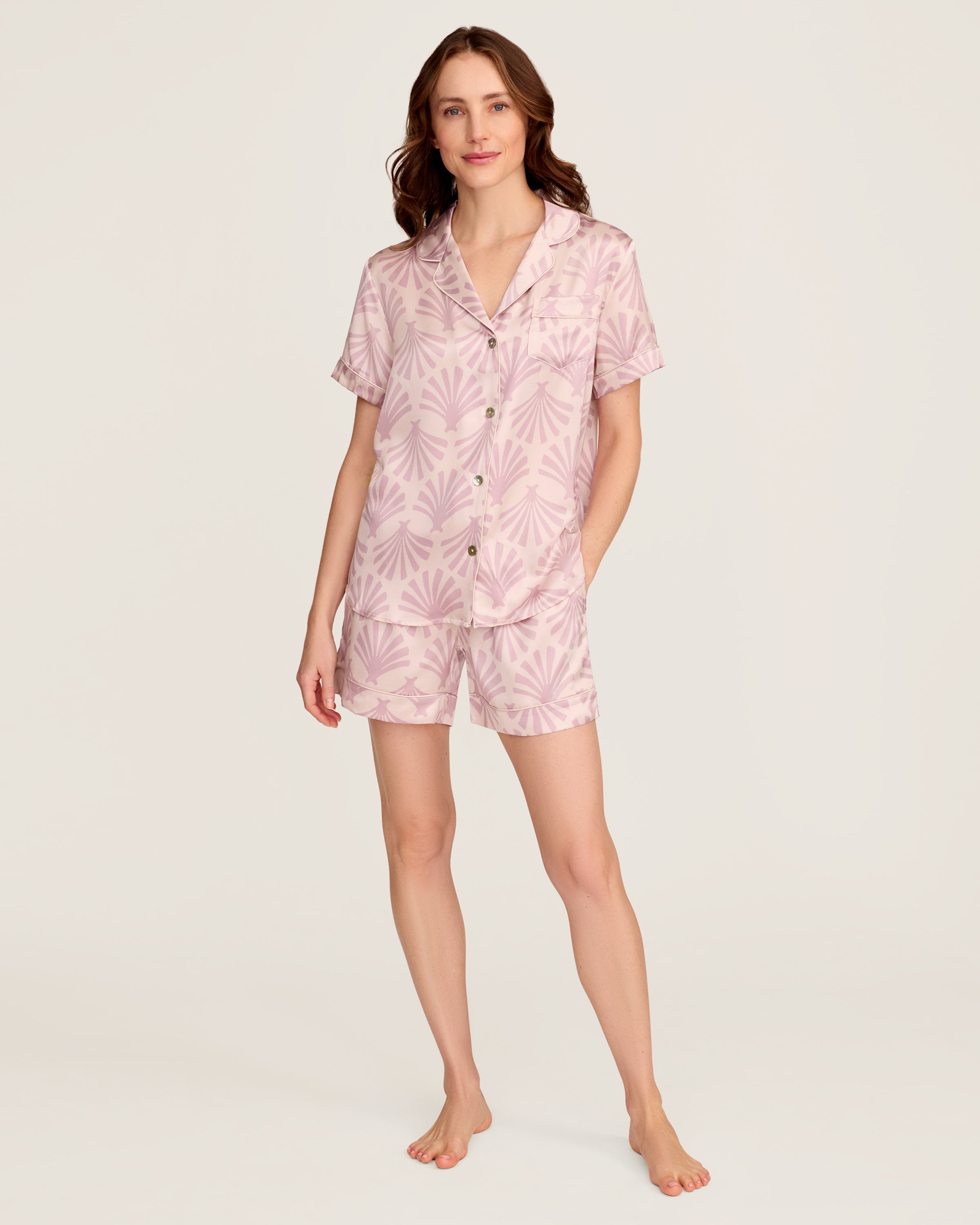 The Women's Silk Short Sleeve Short Set in Blush Tide features a matching pink button-up top and elastic-waist shorts, both adorned with a light purple geometric fan pattern.