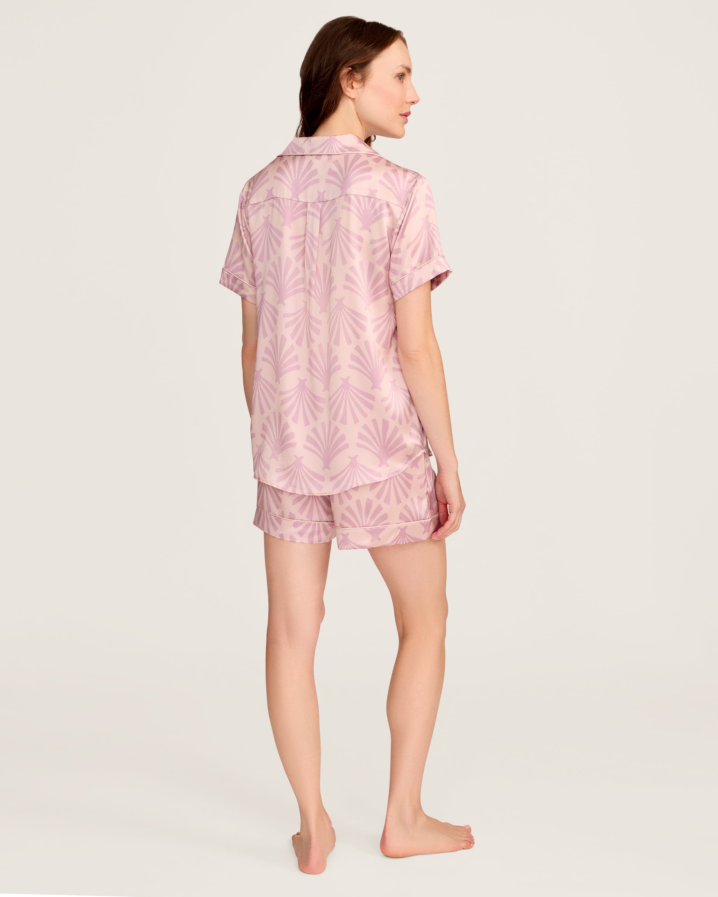 The Women's Silk Short Sleeve Short Set in Blush Tide features a matching pink button-up top and elastic-waist shorts, both adorned with a light purple geometric fan pattern.