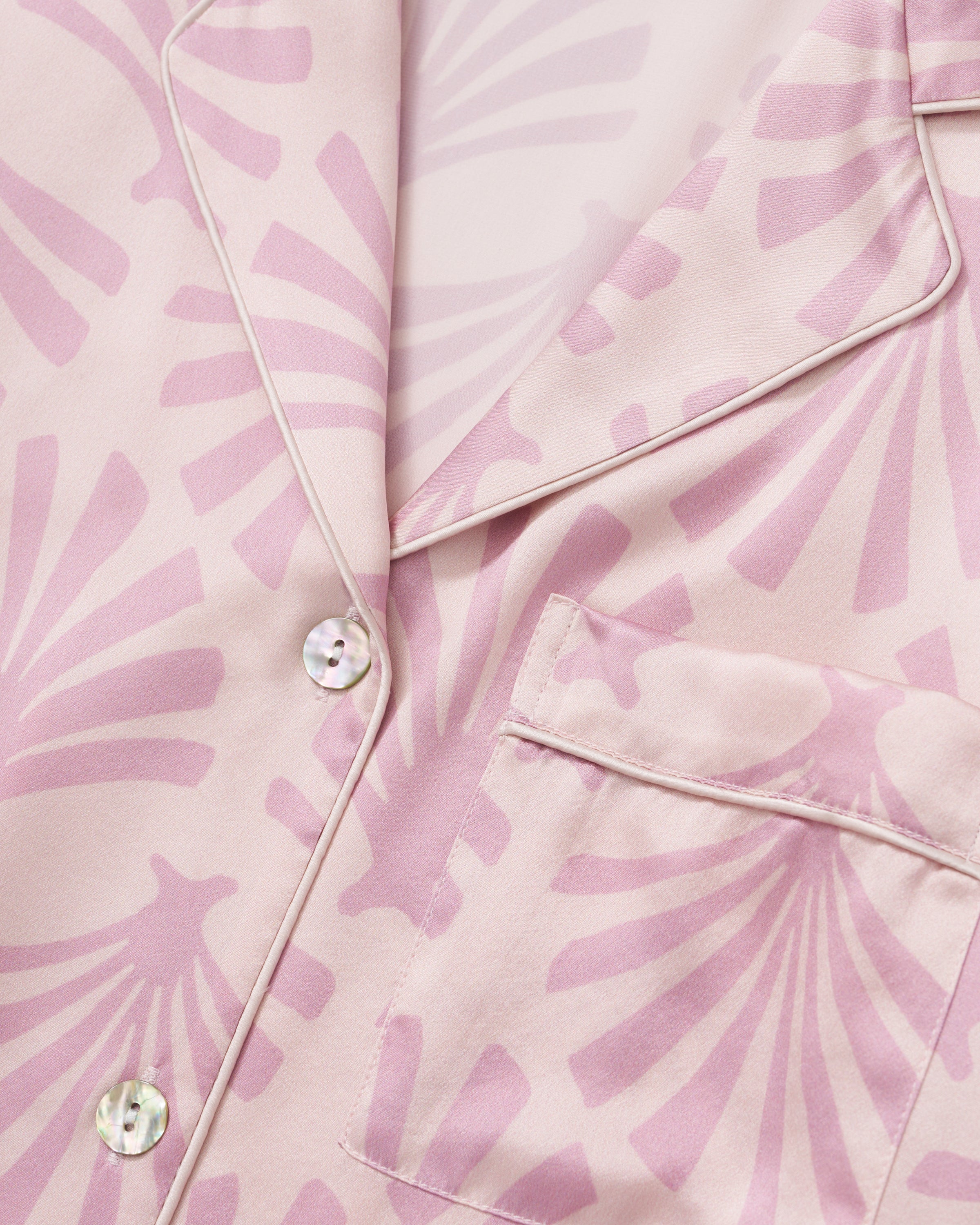 The Women's Silk Short Sleeve Short Set in Blush Tide features a matching pink button-up top and elastic-waist shorts, both adorned with a light purple geometric fan pattern.