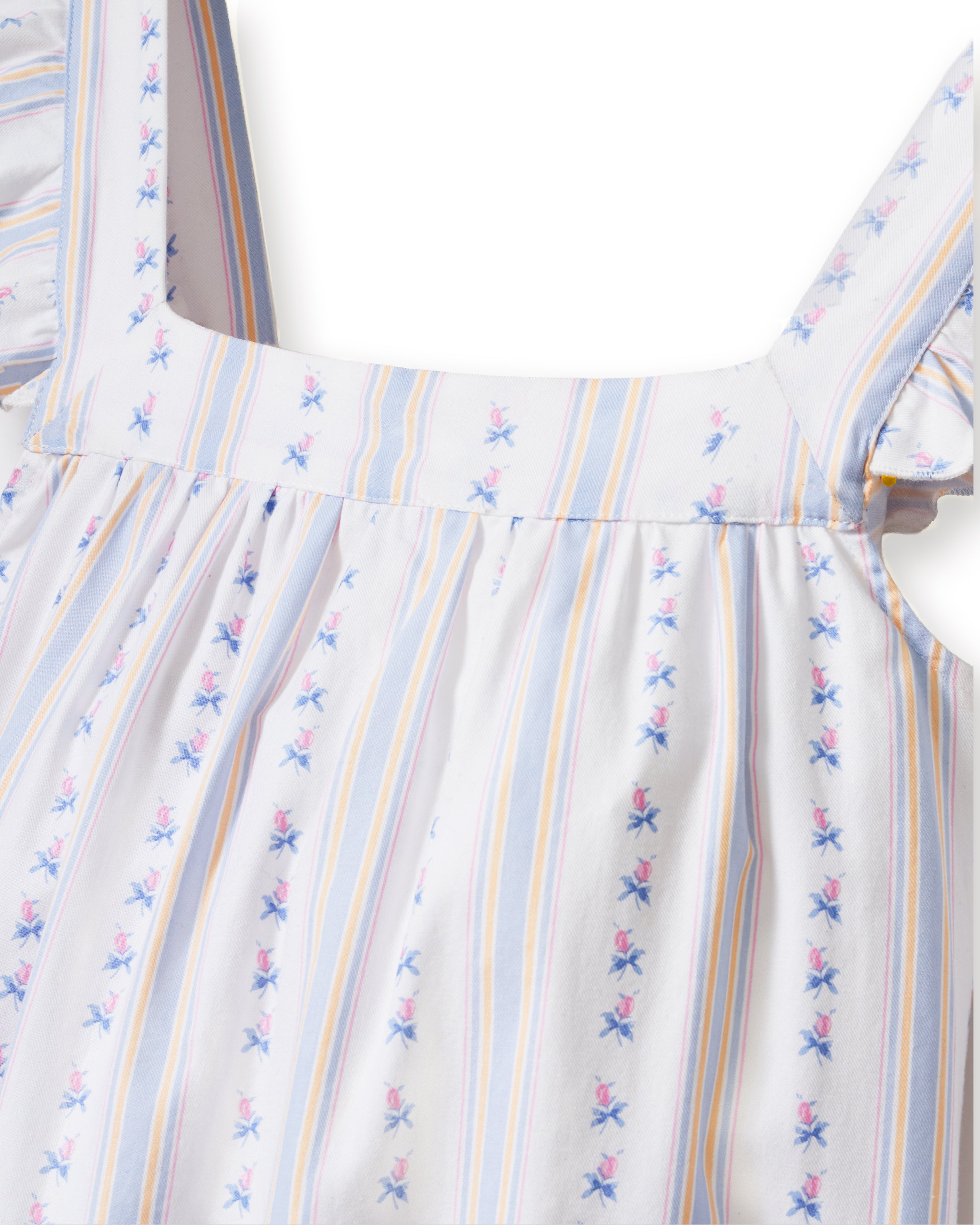 A woman with long curly hair models the Women's Twill Clara Short Set in Cottage Stripe—a loose, sleeveless pajama set with ruffled shoulders and shorts, featuring white fabric with pastel stripes and floral patterns—against a plain background.