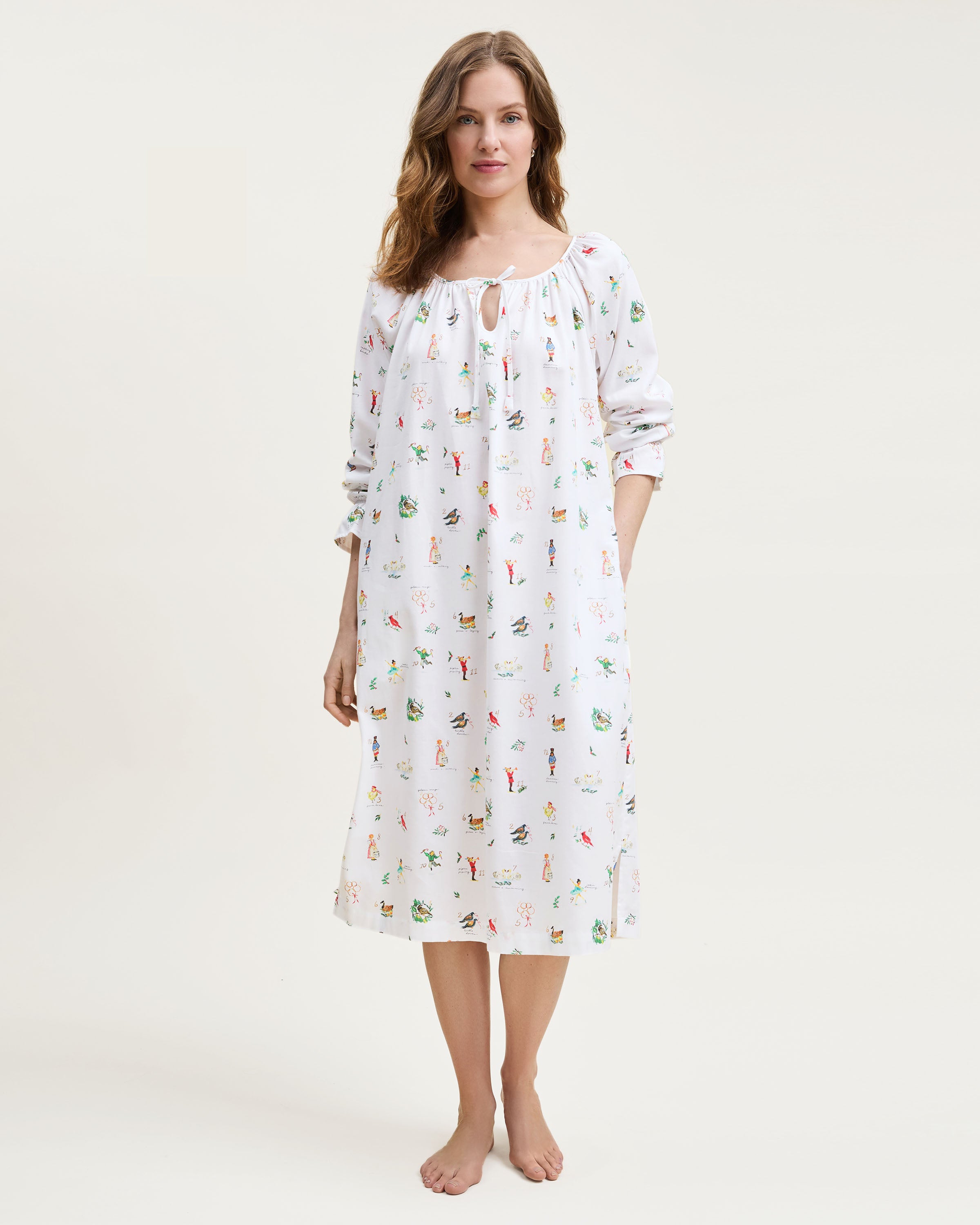 The Women's Twill Delphine Nightgown in 12 Days of Christmas is a white, long-sleeve nightgown with a gathered neckline, small bow tie, and a festive print inspired by the 12 Days of Christmas.
