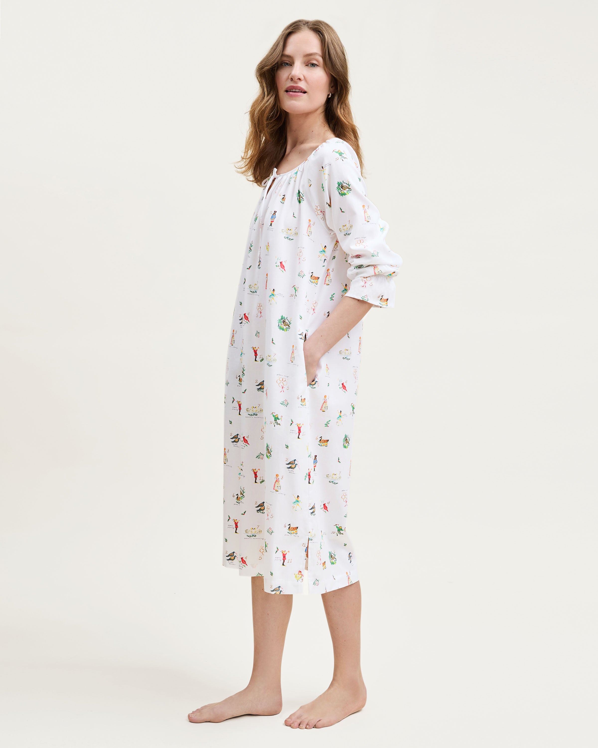 The Women's Twill Delphine Nightgown in 12 Days of Christmas is a white, long-sleeve nightgown with a gathered neckline, small bow tie, and a festive print inspired by the 12 Days of Christmas.