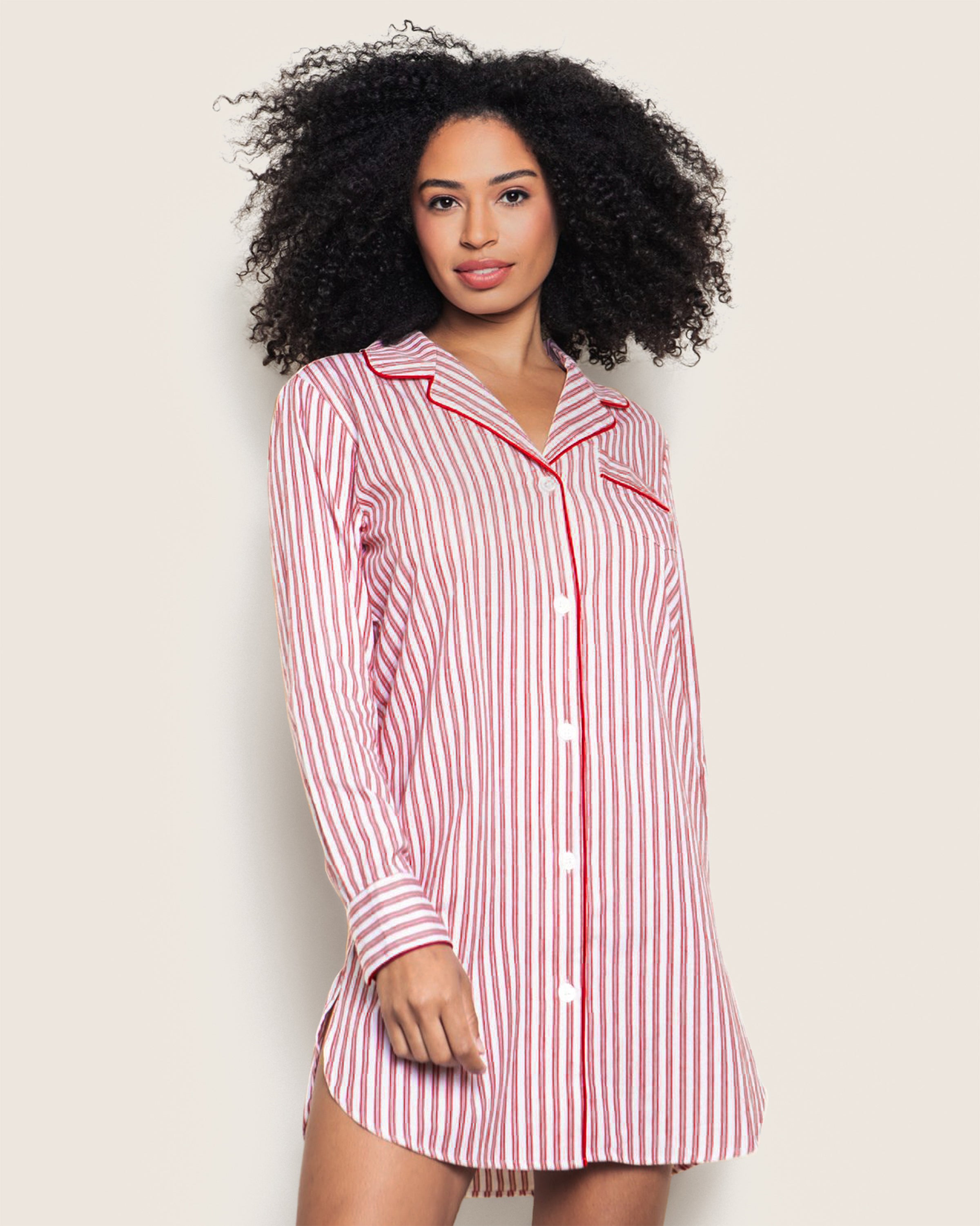 A woman with curly hair wears Petite Plumes Womens Twill Nightshirt in Antique Red Ticking, crafted from premium cotton. Against a plain backdrop, she gazes neutrally at the camera, effortlessly showcasing this timeless piece.