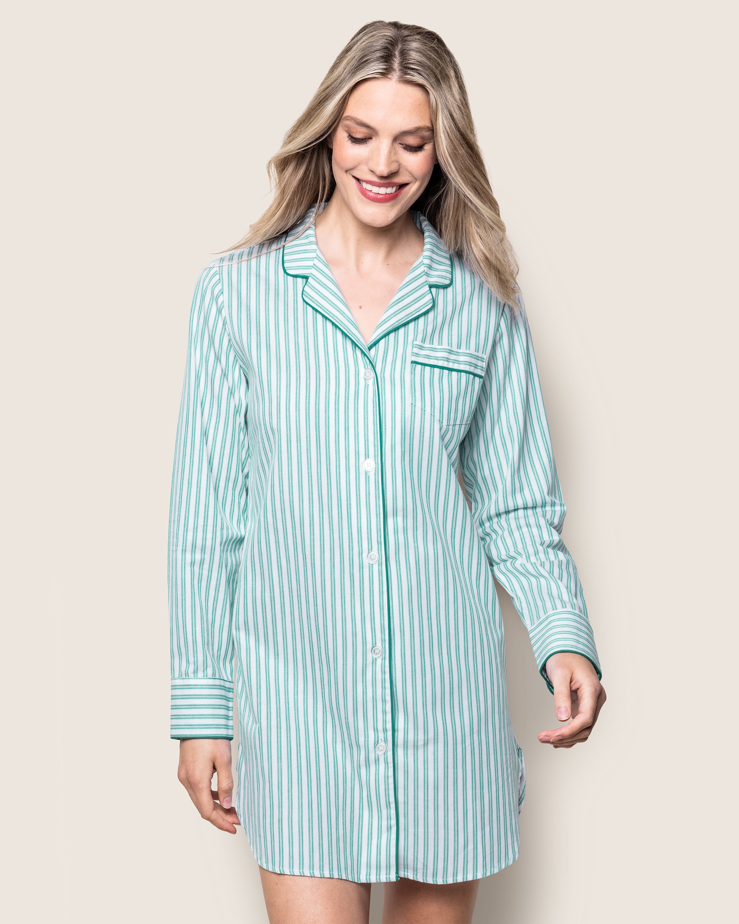 A person smiles while wearing a Petite Plume Womens Twill Nightshirt in Emerald Ticking, looking down against an off-white background.