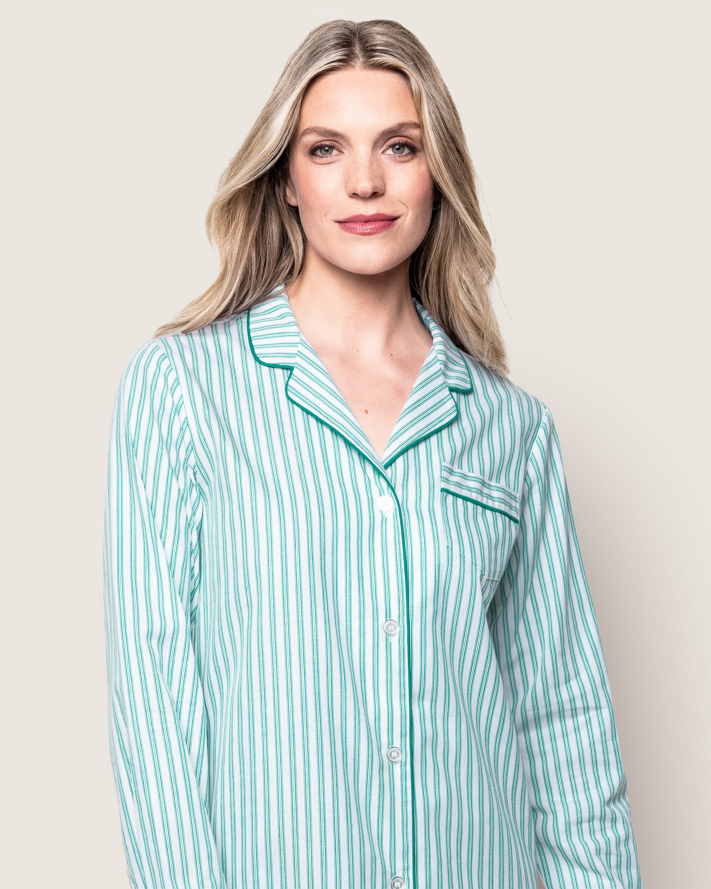 A person with long blond hair stands against a plain background, wearing the Womens Twill Nightshirt in Emerald Ticking by Petite Plume, featuring a classic French ticking pattern.