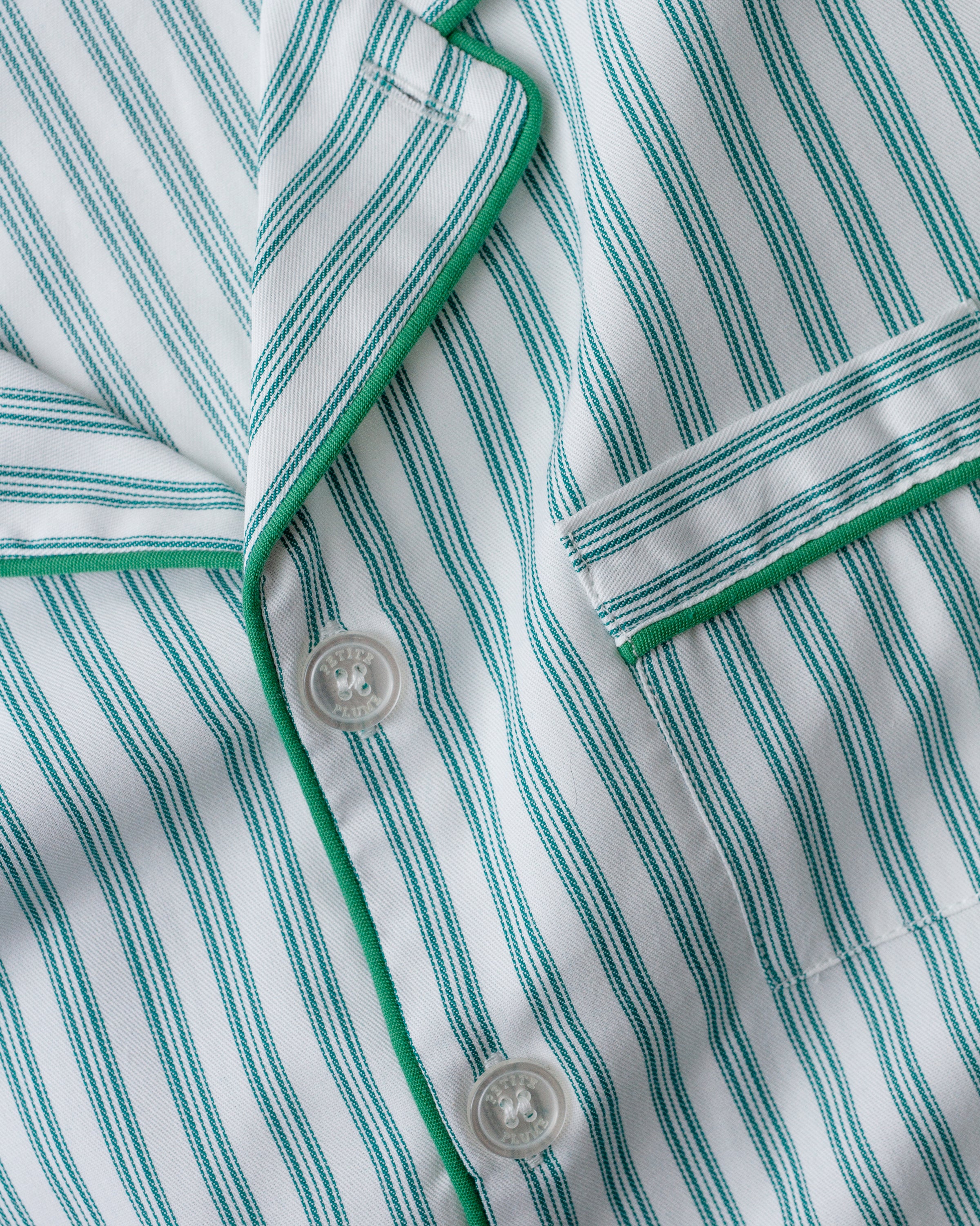 Close-up of Petite Plumes Womens Twill Nightshirt in Emerald Ticking, showcasing vertical green and white stripes. Made from 100% cotton twill, it features white buttons, a pocket, and green piping along the collar and pocket edges.