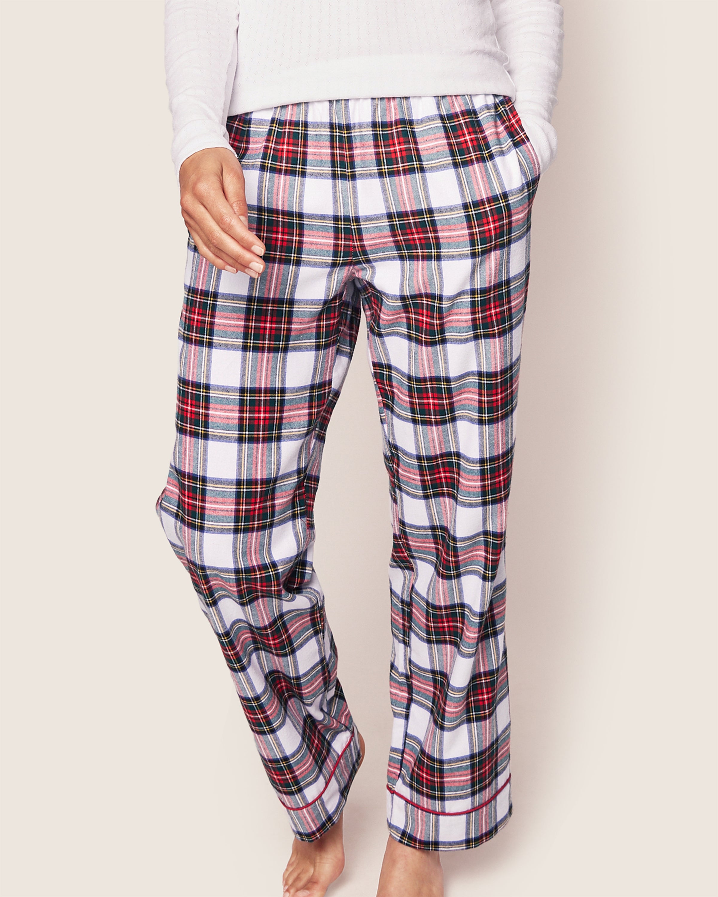 A person wears Petite Plumes Womens Brushed Cotton Pants in Balmoral Tartan, capturing Scottish tradition. One hand rests in a pocket against an off-white backdrop, highlighting the luxurious and timeless appeal of this sleepwear.