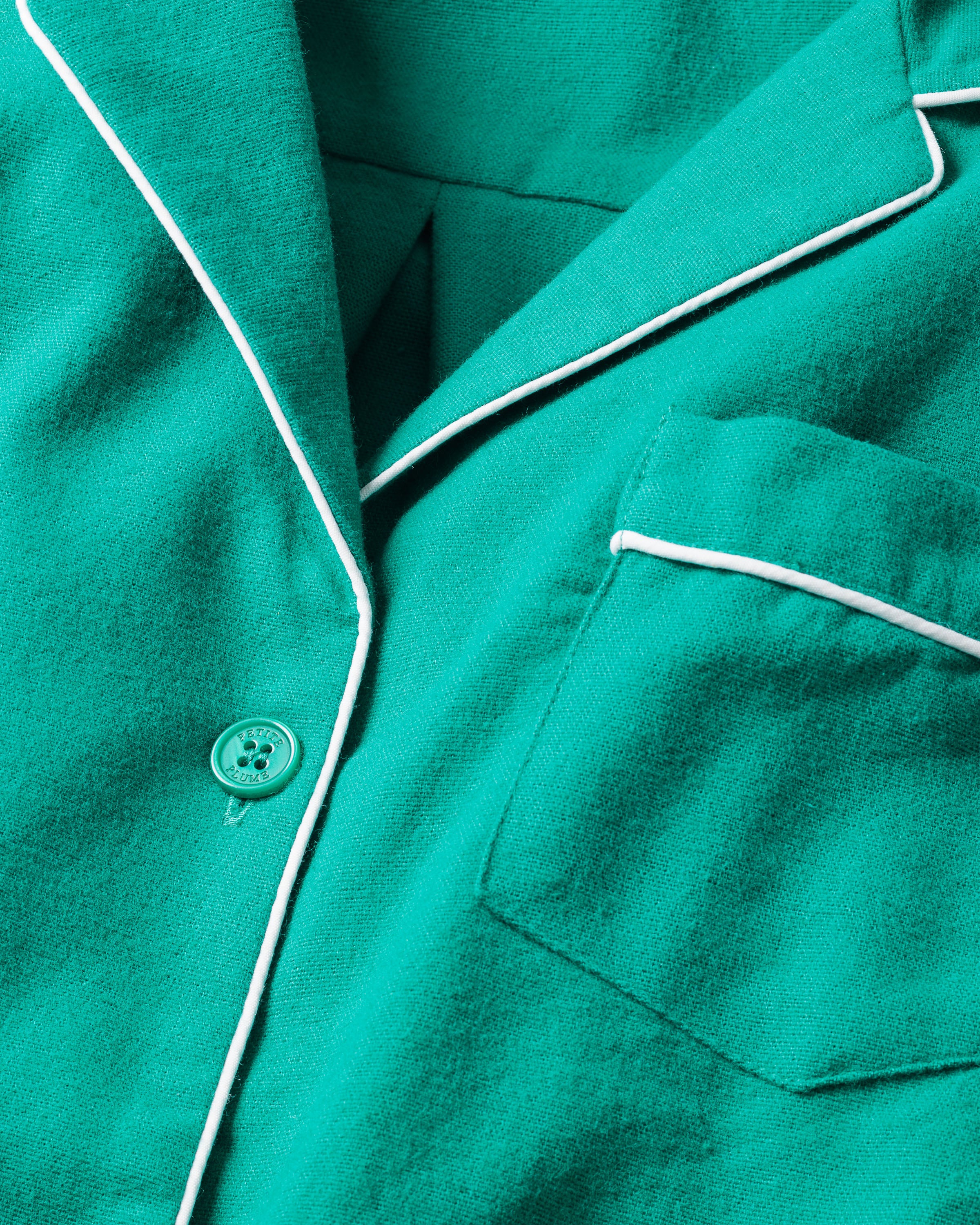 Close-up of a Womens Flannel Pajama top in Forest Green by Petite Plume with white piping. Made from 100% cotton twill, it includes a chest pocket and single button. The soft fabric promises warmth and comfort.