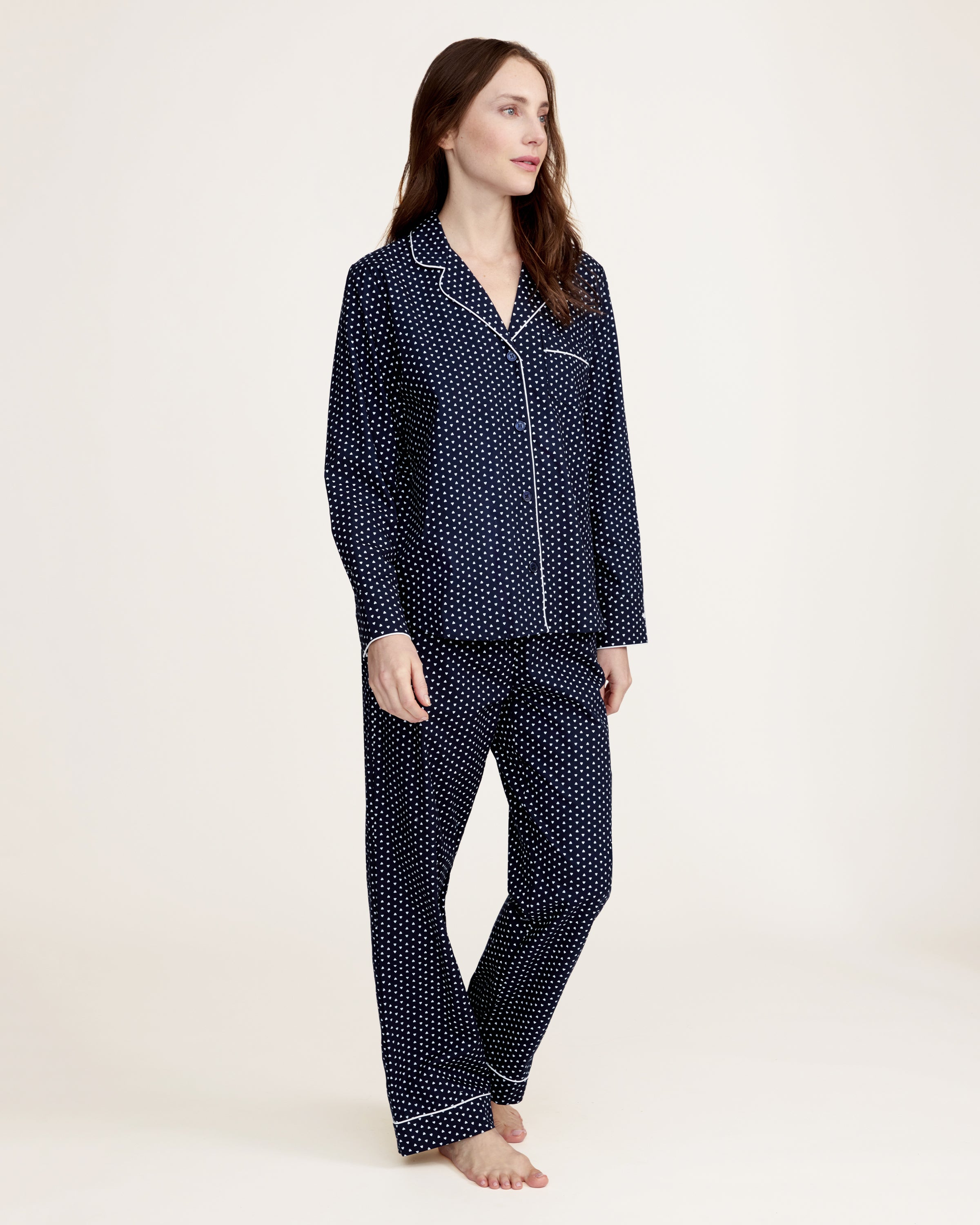 The Women's Twill Pajama Set in Midnight Hearts features a navy blue, long-sleeve top with a collar, button-down front, white heart print, and white piping on the edges and pocket, paired with matching pants.