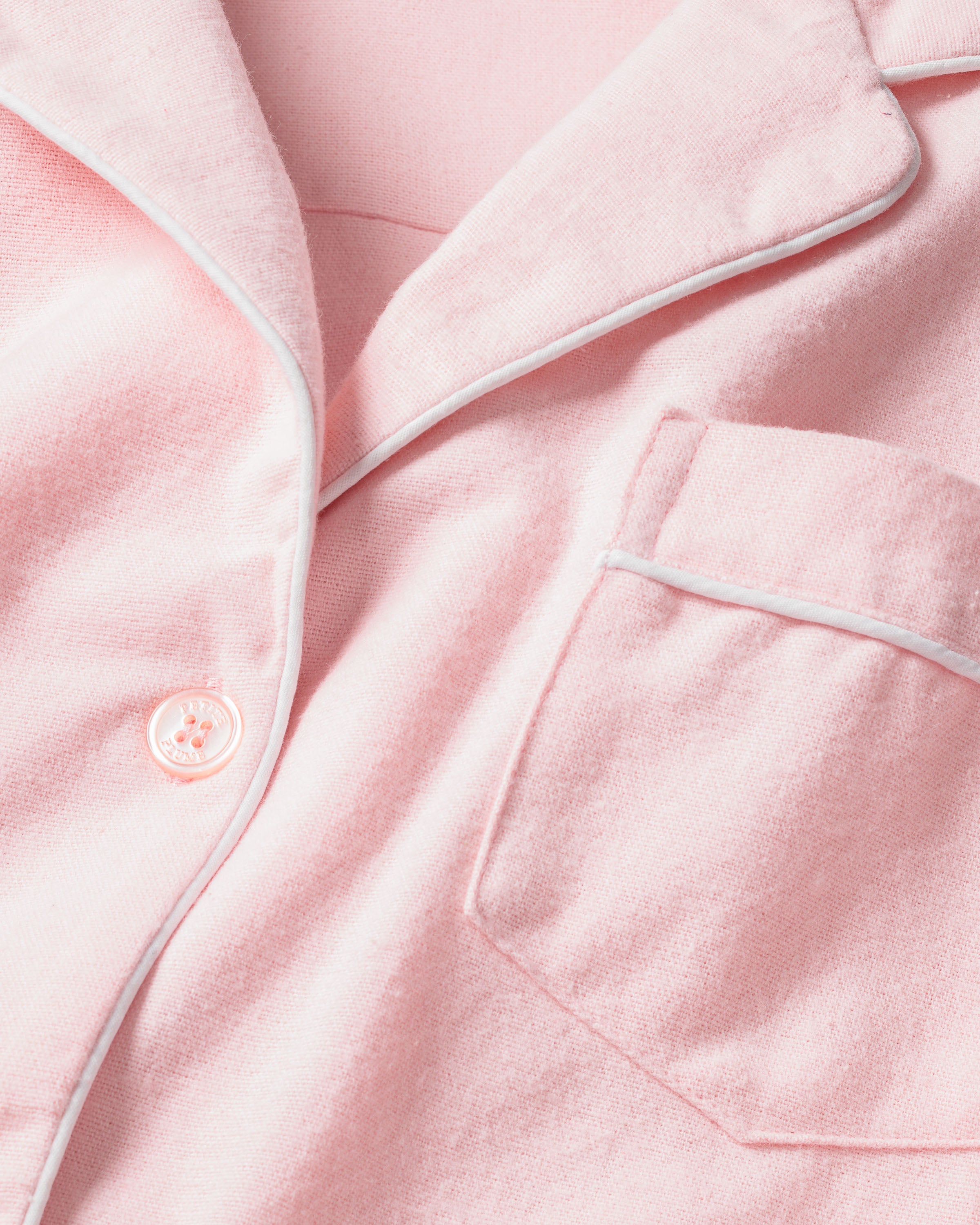 The Womens Flannel Pajama Set in Pink by Petite Plume features a classic design with white piping, a button-up front, collar, and pocket. It embodies timeless sleepwear style and ensures comfort with its soft 100% flannel fabric.