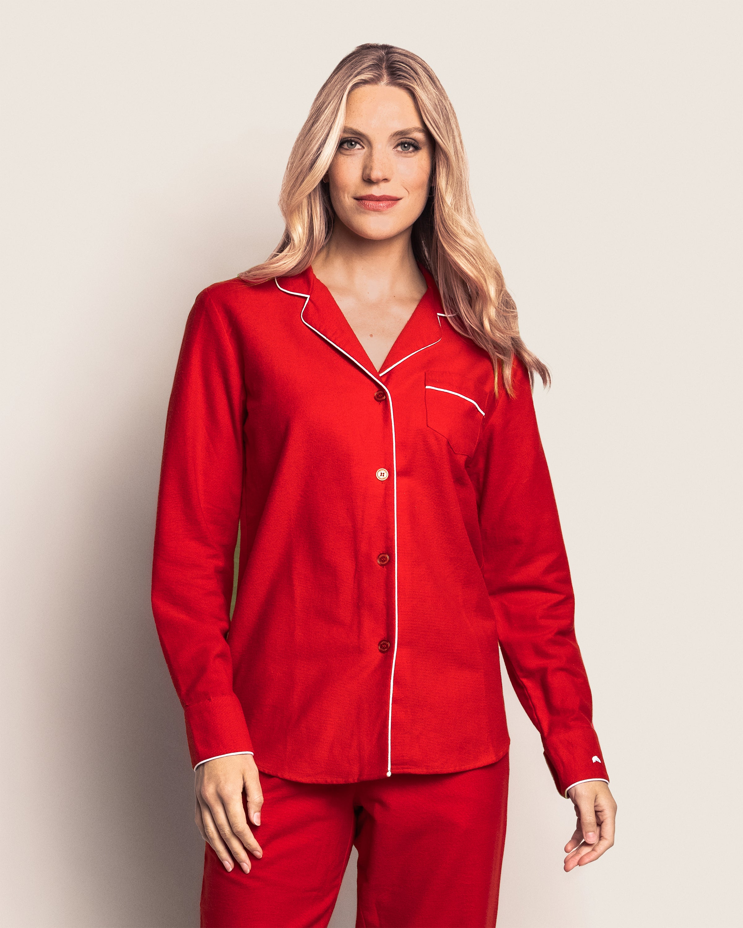 A woman with long blonde hair wearing the Womens Flannel Pajama Set in Red by Petite Plume stands against a plain background. The cozy set, made from soft cotton, includes a top with buttons and a pocket on the left chest.