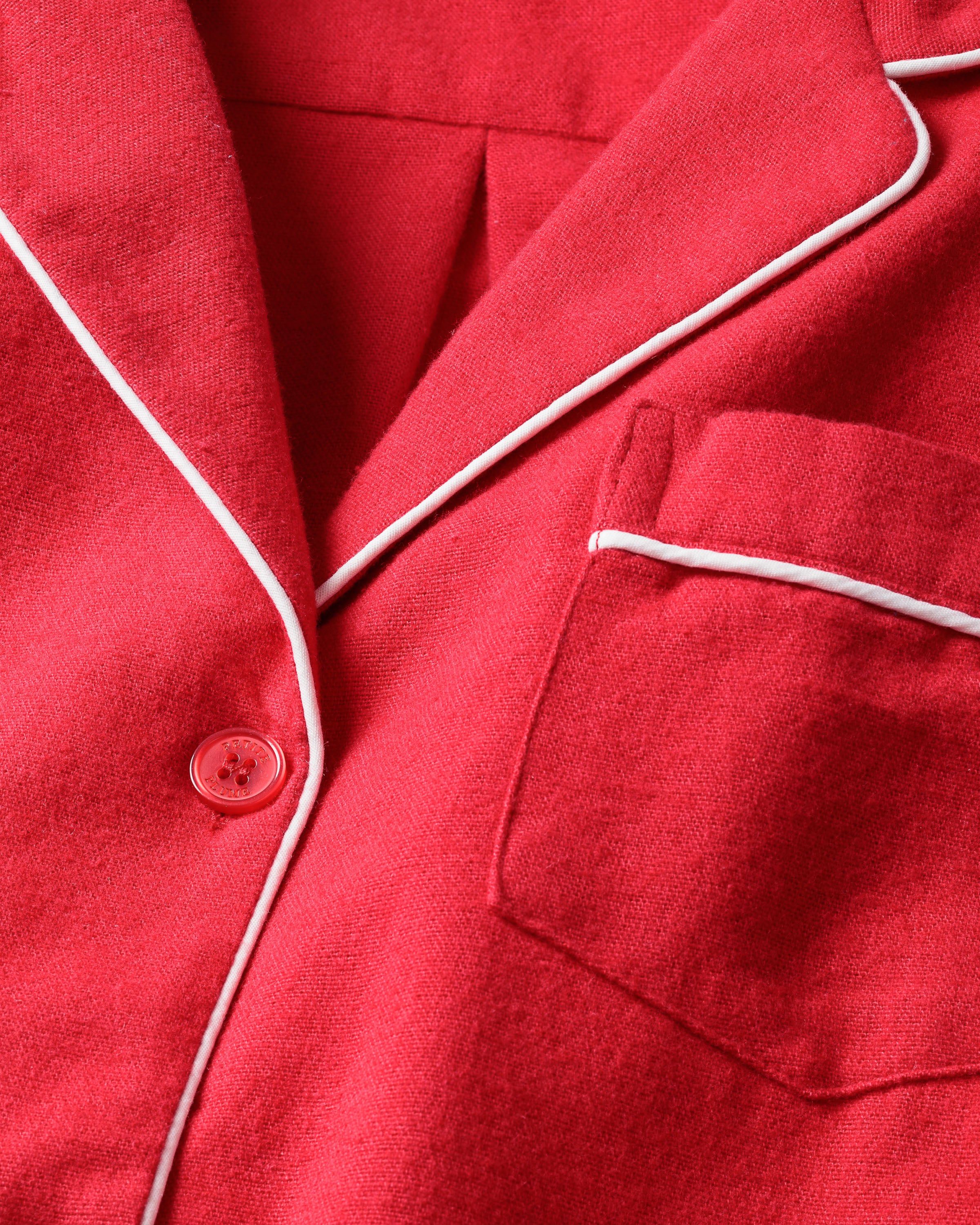 Close-up of the Womens Flannel Pajama Set in Red by Petite Plume, showcasing red flannel fabric with white piping, a chest pocket, and a single red button. The soft and smooth texture suggests it is part of a cozy pajama set.