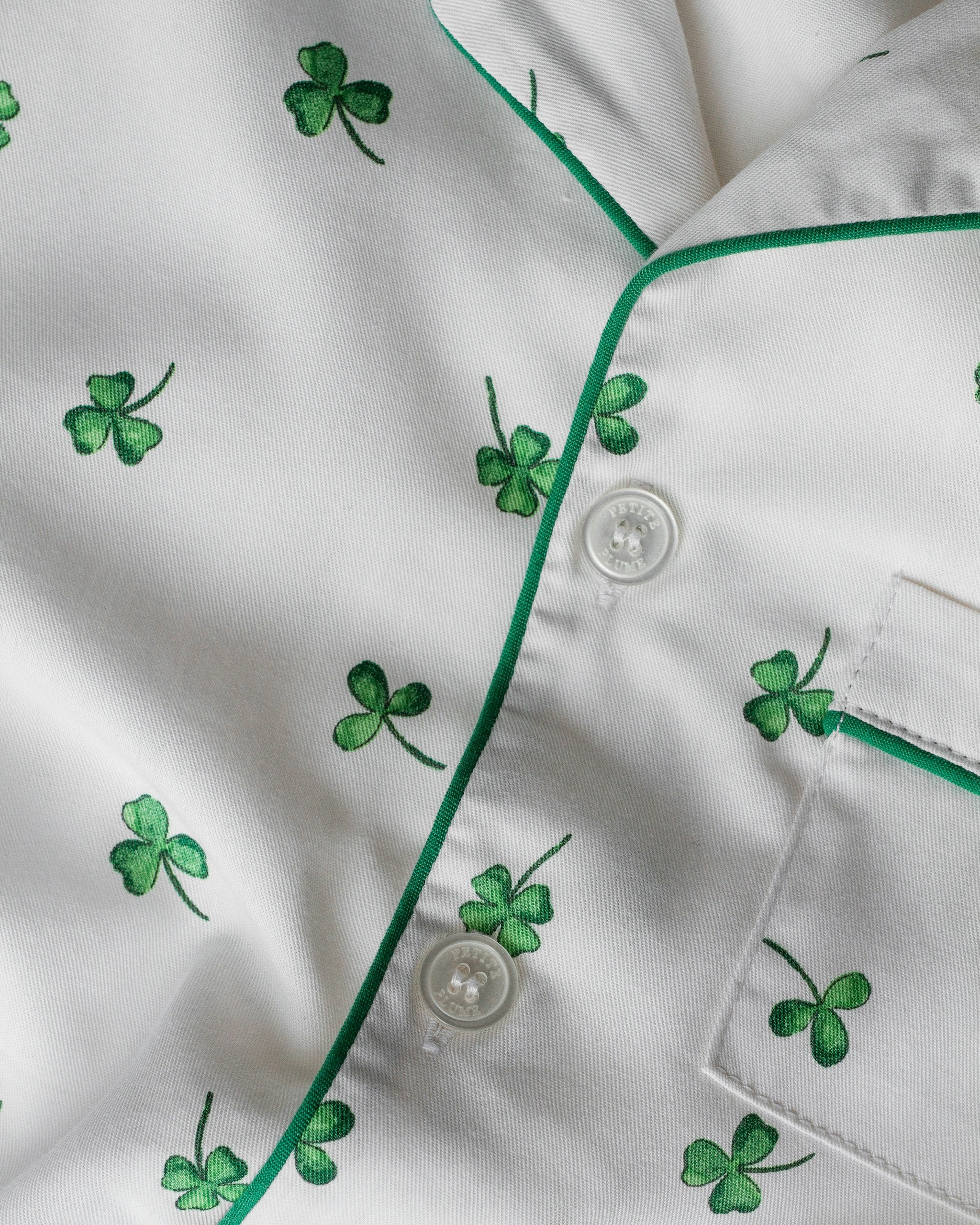 A women's pajama set with a white twill fabric featuring a green shamrock print, including a long-sleeved shirt and pants with a drawstring.