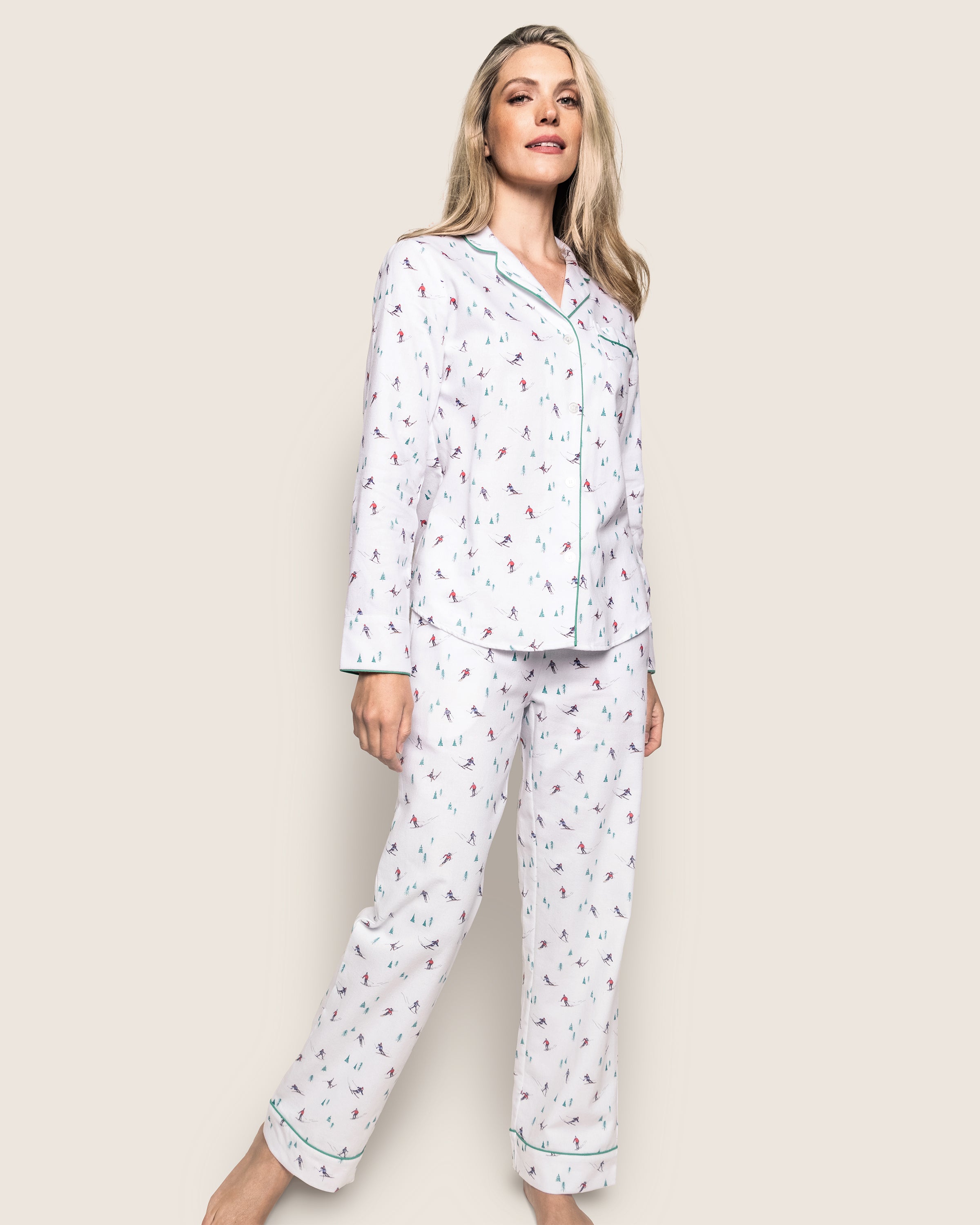 A woman in Petite Plumes Womens Flannel Pajama Set in Après Ski smiles while standing. The collared top has buttons, and the full-length pants promise comfort in brushed cotton flannel. Her long blonde hair cascades against a plain background, enhancing the serene scene.