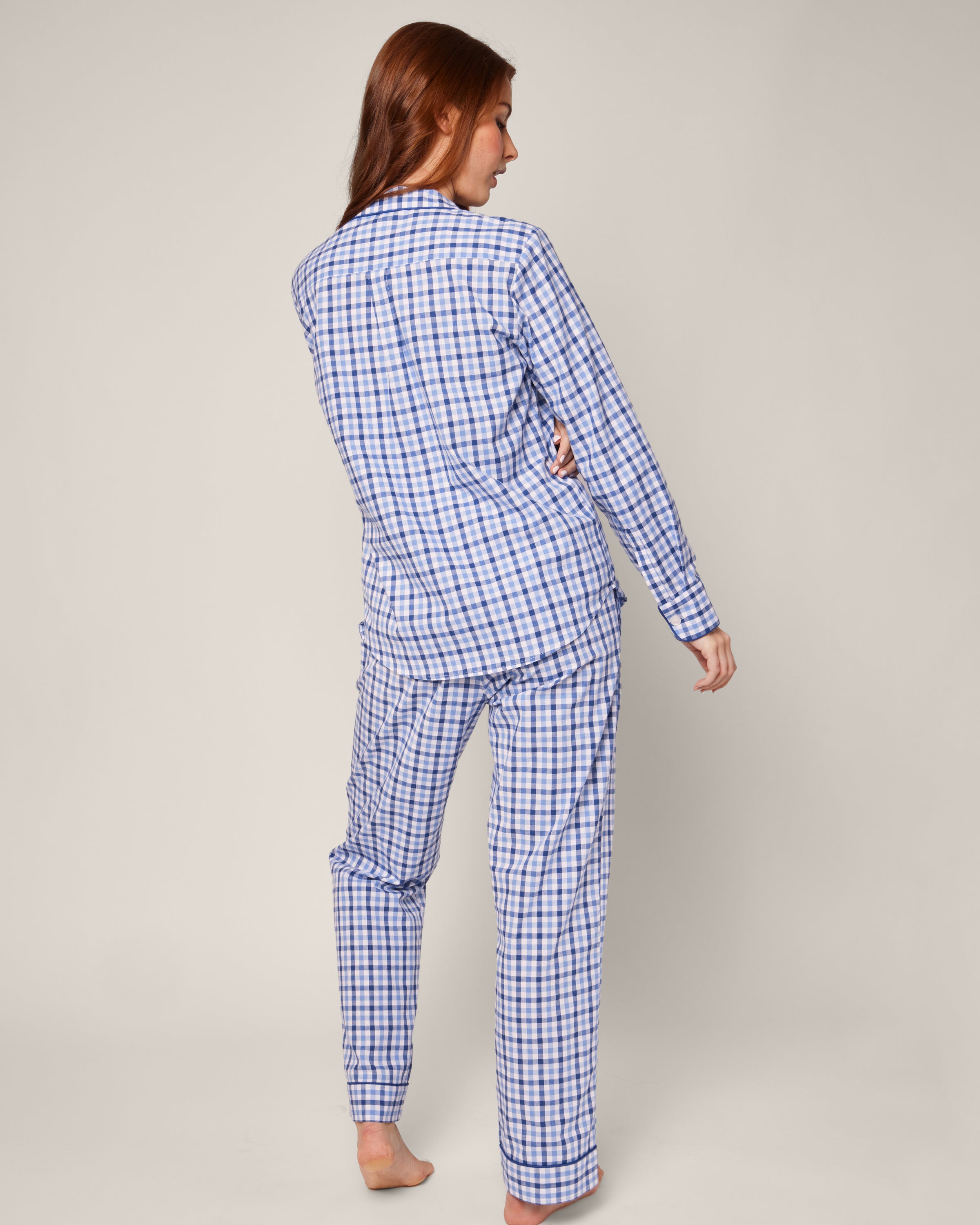 A woman with long red hair models the Womens Twill Pajama Set in Royal Blue Gingham by Petite Plume, standing barefoot and facing away with her head turned to the side against a light plain background.