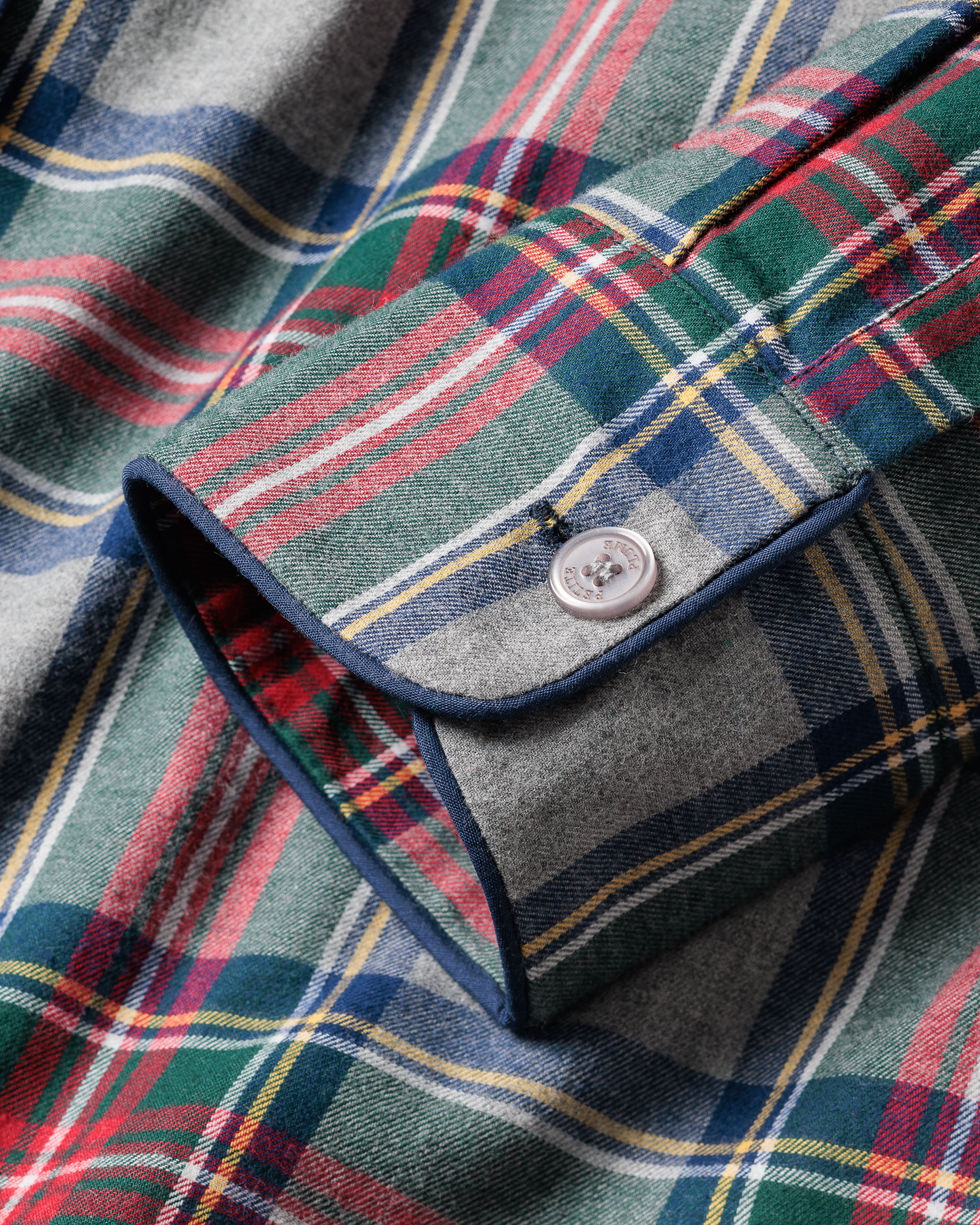 Zoomed-in view of a Womens Brushed Cotton Pajama Set cuff in Westminster Tartan by Petite Plume. The cuff, crafted from 100% cotton, displays a classic tartan design with red, green, blue hues and yellow accents. It features a white button and navy blue piping with detailed stitching.