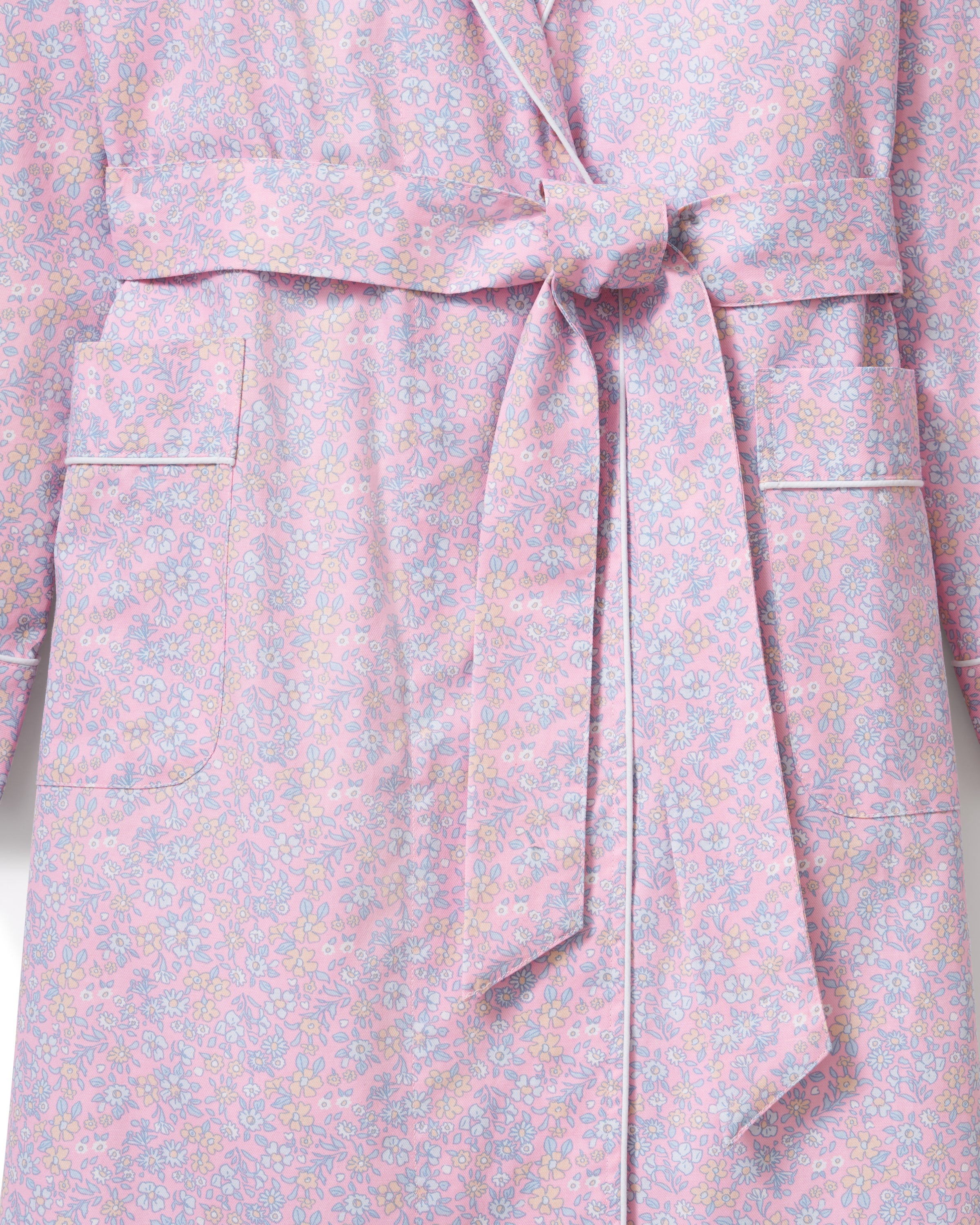 A woman stands barefoot against a plain light background, wearing the Women's Twill Robe in Fleur Blush—a knee-length, long-sleeved, light pink robe with a subtle floral pattern and waist tie.