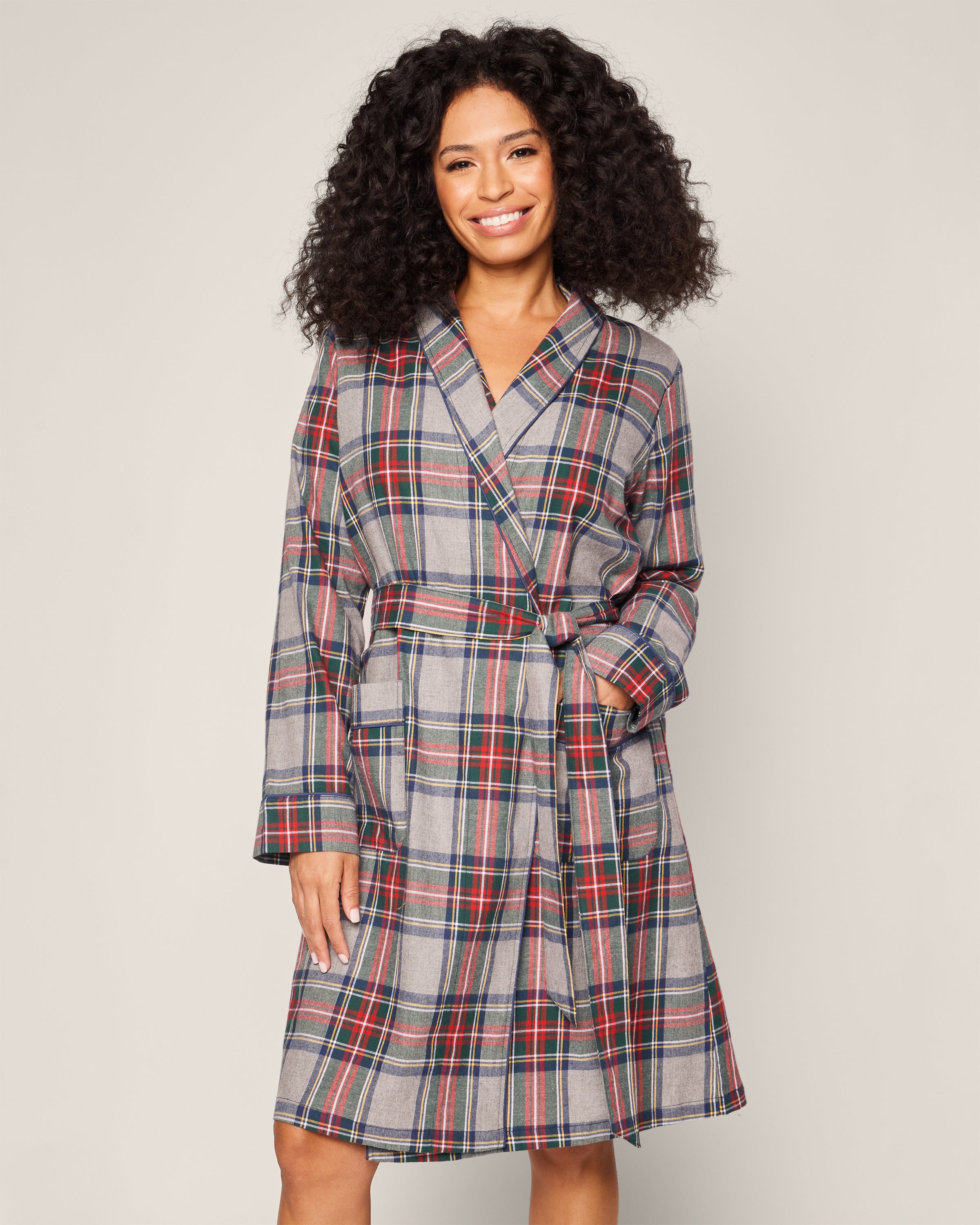 A woman shines in collectible sleepwear, her Petite Plume Womens Brushed Cotton Robe in Westminster Tartan featuring red, green, and blue tones. Her curly hair frames her face against a neutral backdrop, evoking the timeless elegance of Scottish tradition.