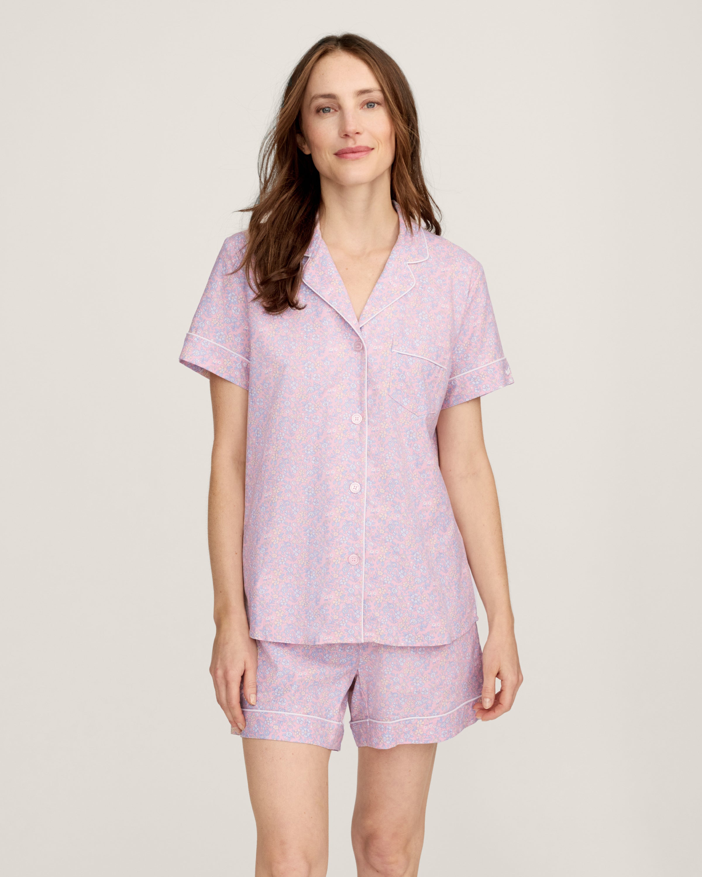 A woman with long brown hair is wearing the Women's Twill Short Sleeve Short Set in Fleur Blush and smiling softly, standing in front of a plain light background.