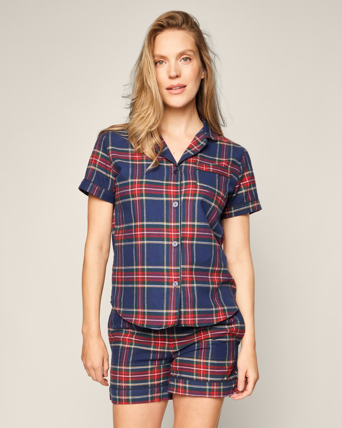 Against a plain light background, a person with long hair is wearing a matching Windsor Tartan pajama set in brushed cotton by Petite Plume.