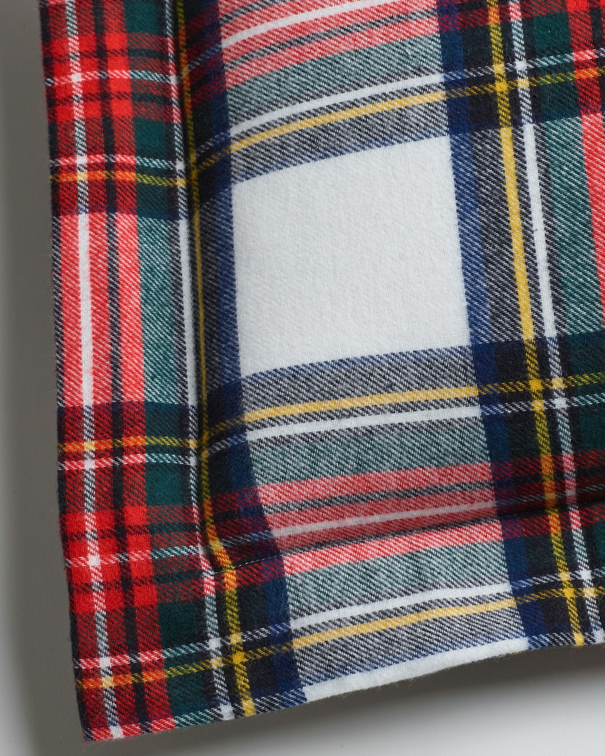 A close-up of the Plush Decorative Pillow in Balmoral Tartan by Petite Plume shows vibrant red, green, blue, yellow, and white patterns. Its traditional tartan print features colorful intersecting lines for a cozy and classic look, perfect for adding holiday flair.