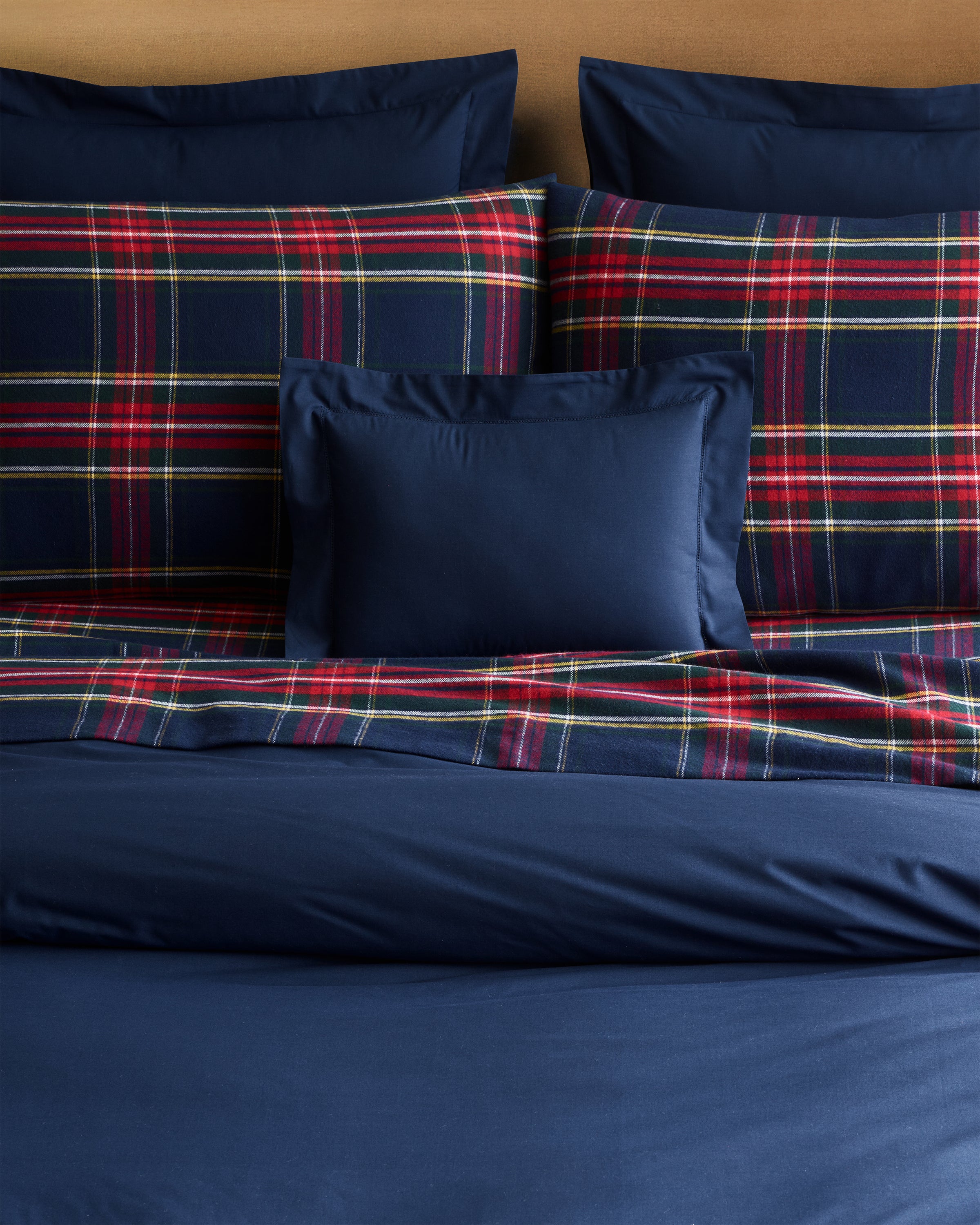 Petite Plumes bedding includes a navy and red plaid percale duvet cover with pillows featuring a plaid pattern accented with green, yellow, and white stripes. A Decorative Pillow in Navy completes the look by sitting in front of the larger plaid pillows.