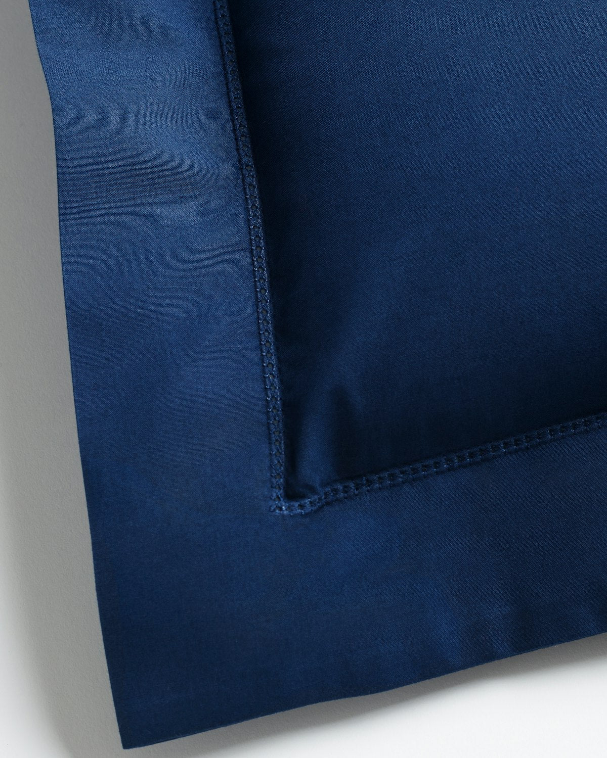 Close-up of a Decorative Pillow in Navy by Petite Plume, featuring visible stitching along the edges in percale fabric, displayed on a light surface.