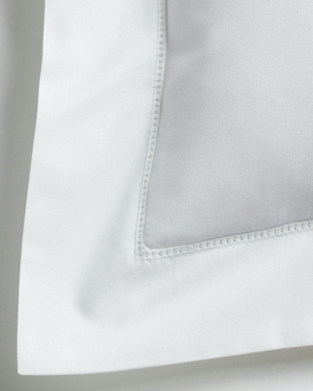 A close-up of Petite Plumes Decorative Pillow in White shows a neatly stitched percale corner. The crisp, smooth material complements the white background, enhancing its simple elegance.