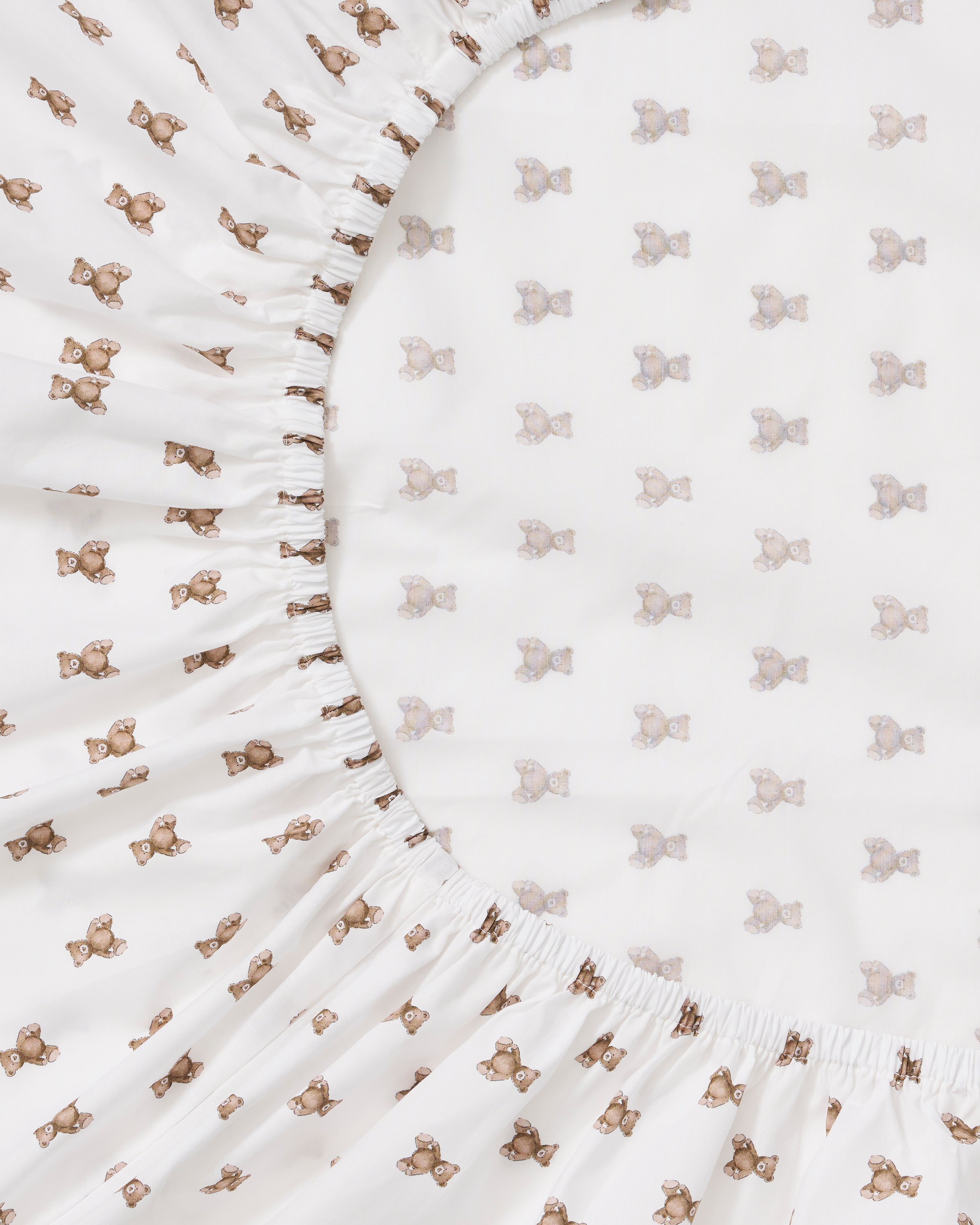 A close-up of the Luxe Premium Percale Crib Sheet in Teddy Tales, featuring a small repeating brown and orange floral pattern on white, smoothly wrapped around a mattress corner.